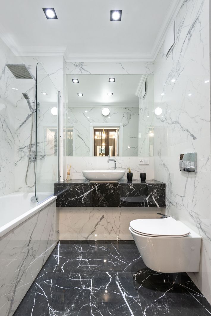 Modern white marble bathroom with black floor tile, bathtub, sink, and wall mirror.