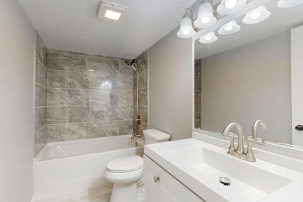 Modern bathroom with gray tile shower, white tub, and vanity with large mirror and lights
