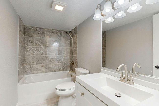 Bright modern bathroom with tub, large mirror, double vanity, and gray tiled shower wall