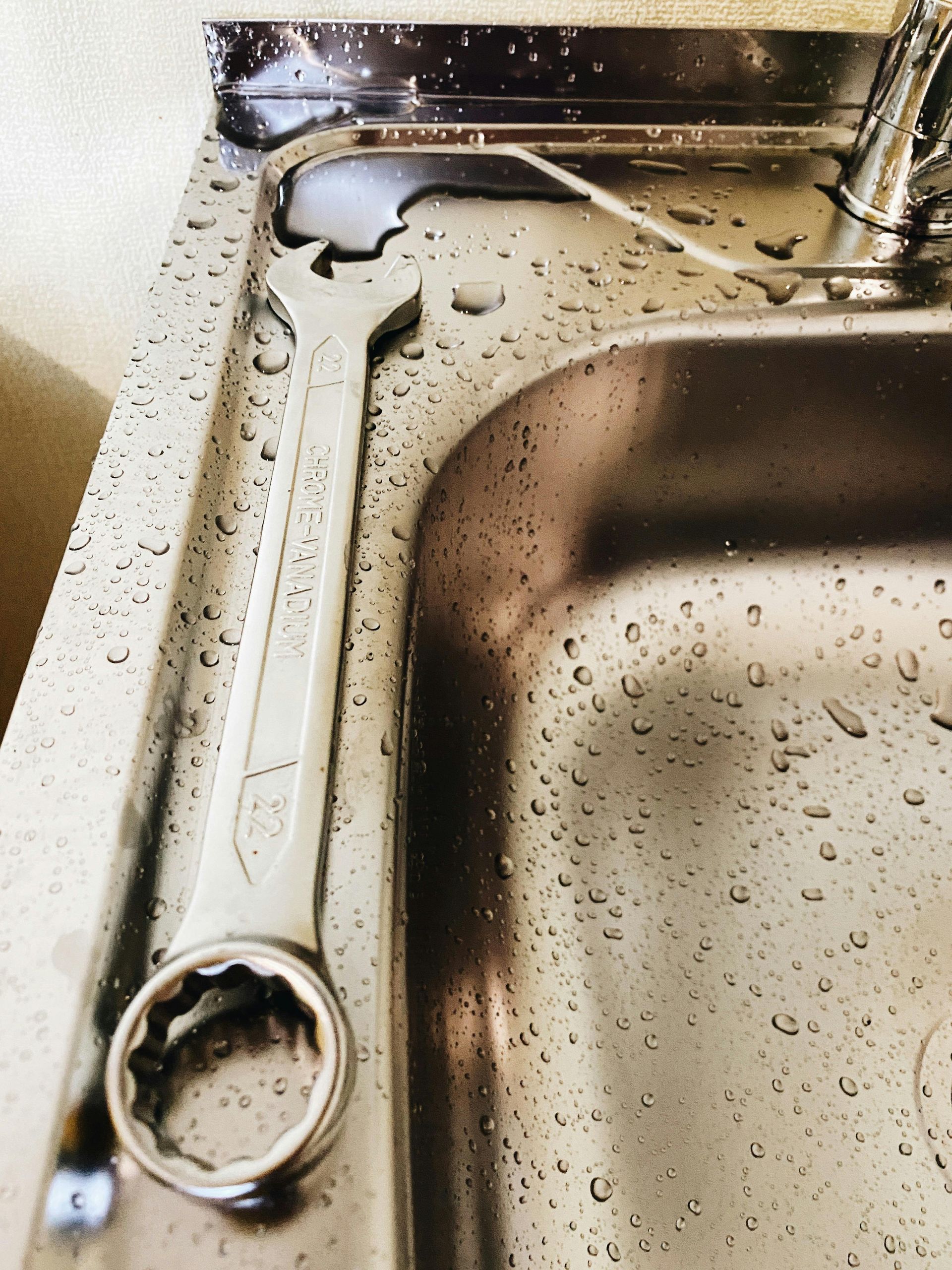 A wrench is laying on a stainless steel sink