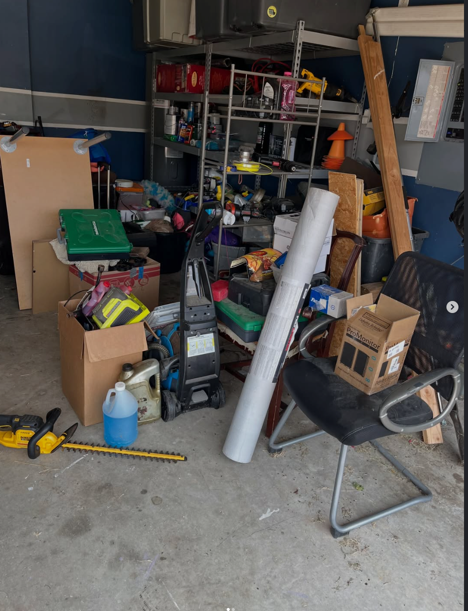 Cluttered garage with shelves of tools, boxes, and supplies, plus a chair and large white tube on the floor