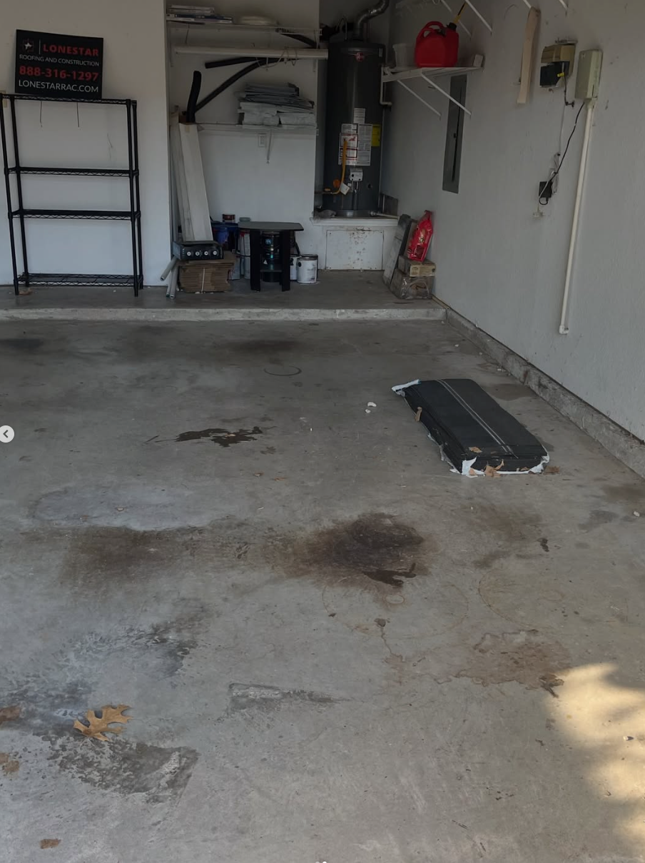 Empty garage with concrete floor, shelves, water heater, and scattered stains near the back wall