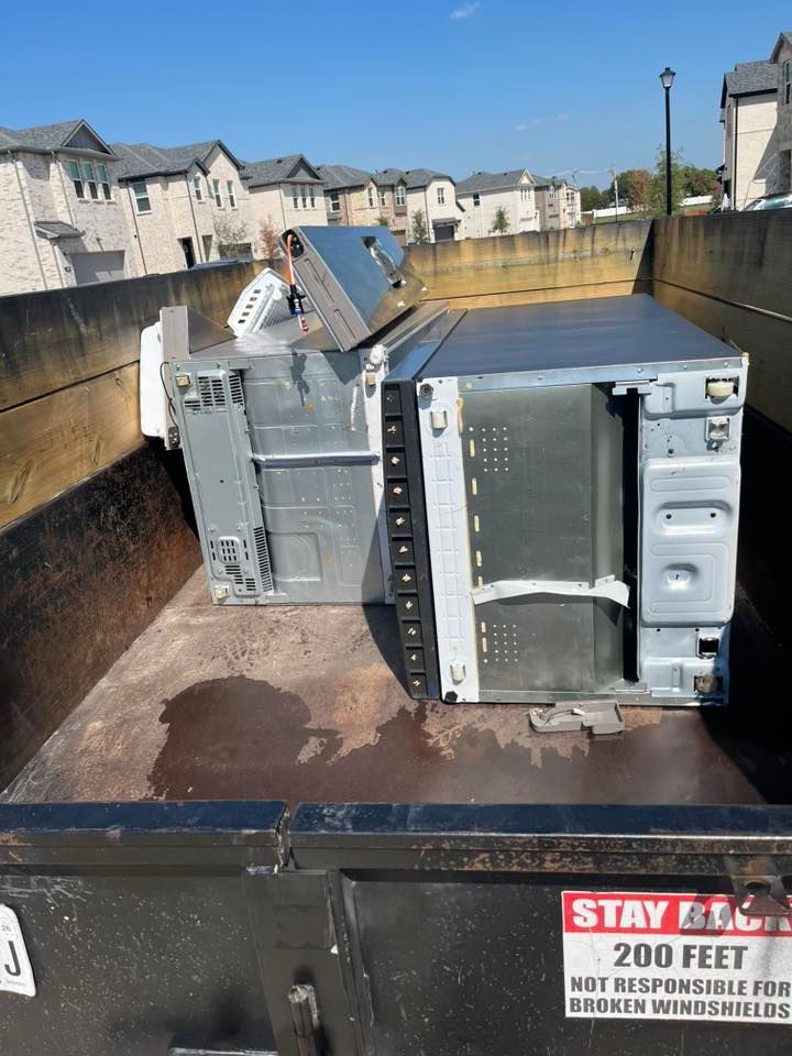 Broken appliance parts in a dumpster on a sunny residential street with townhouses in the background