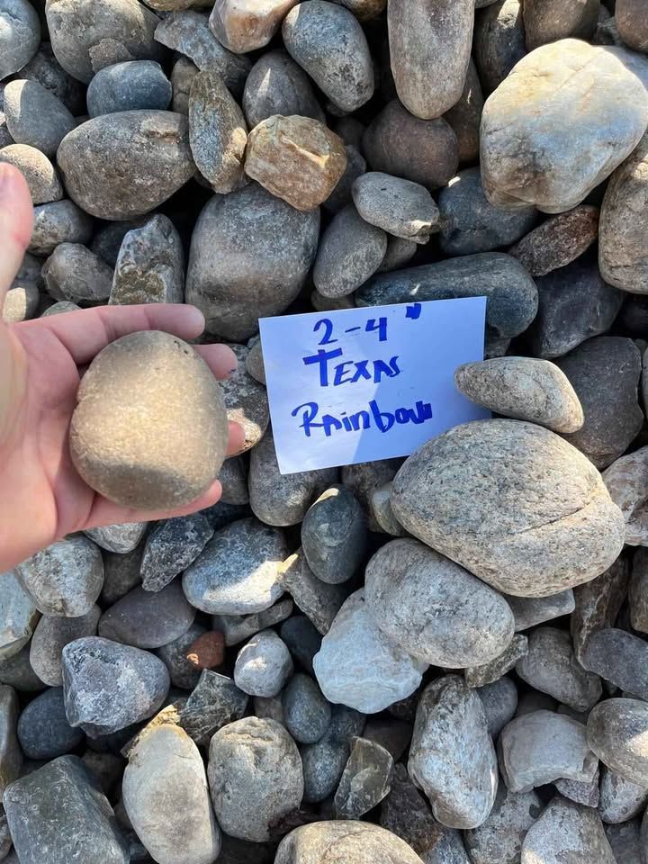 Hand holding a tan rock over a pile of gray stones beside a note reading “2-4 Texas Rainbow”