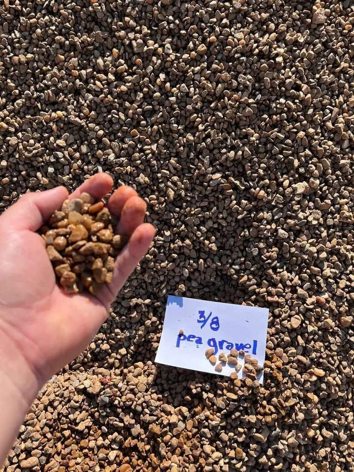 Hand holding brown pebbles beside a handwritten sign reading “3/8 pea gravel.”