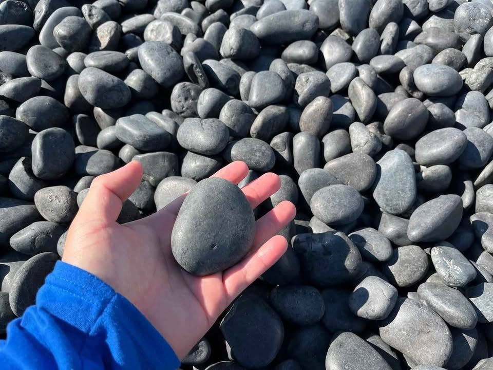 Hand holding a smooth gray pebble over a bed of dark gray stones