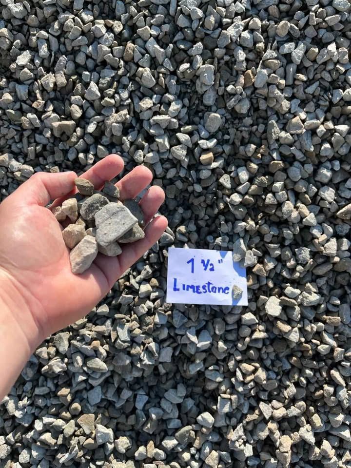 Hand holding gray limestone rocks over a gravel pile, with a handwritten “1 yd Limestone” label.