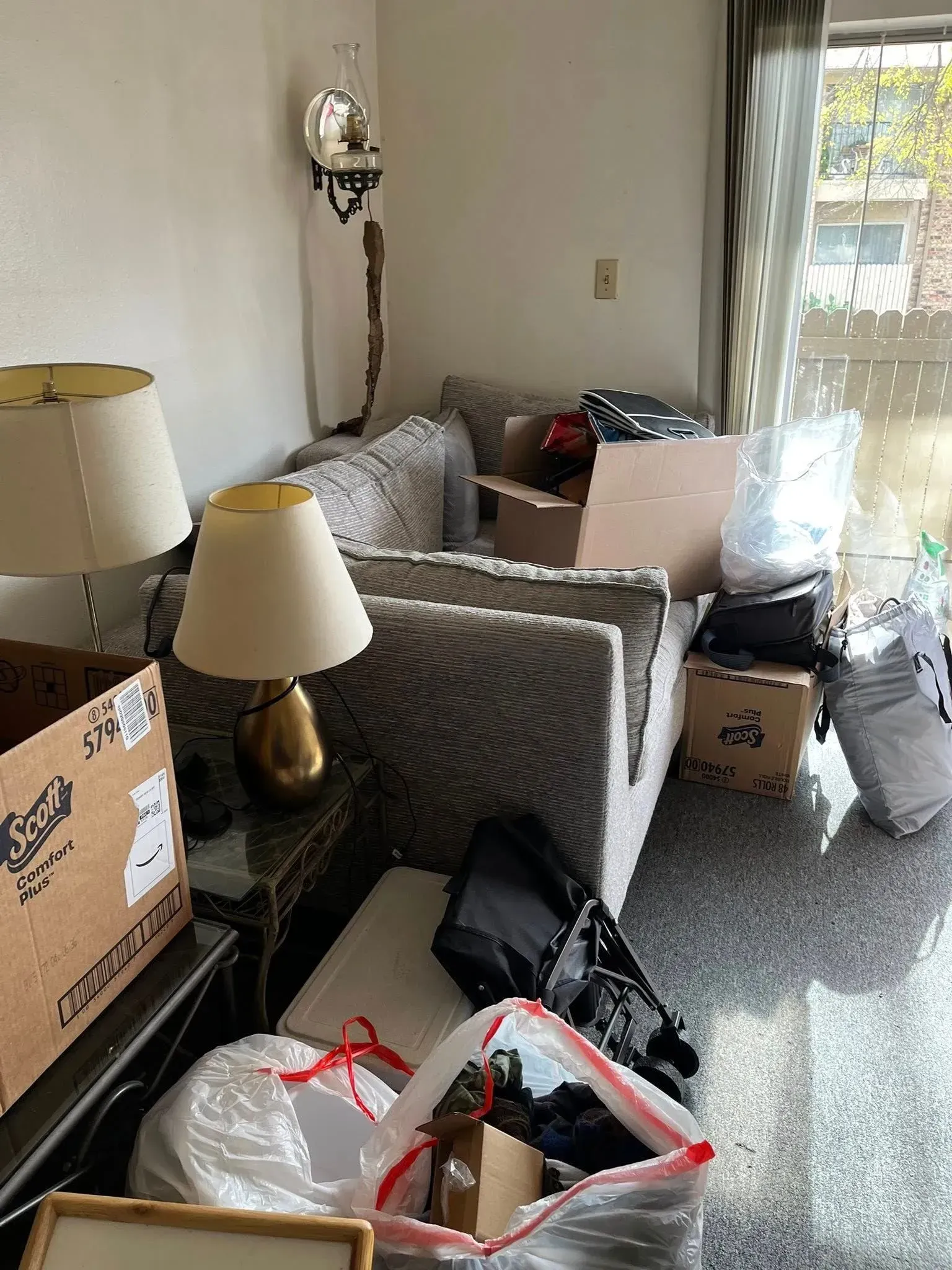 Cluttered room with boxes, lamps, chairs, and a bed near a bright window and sliding door