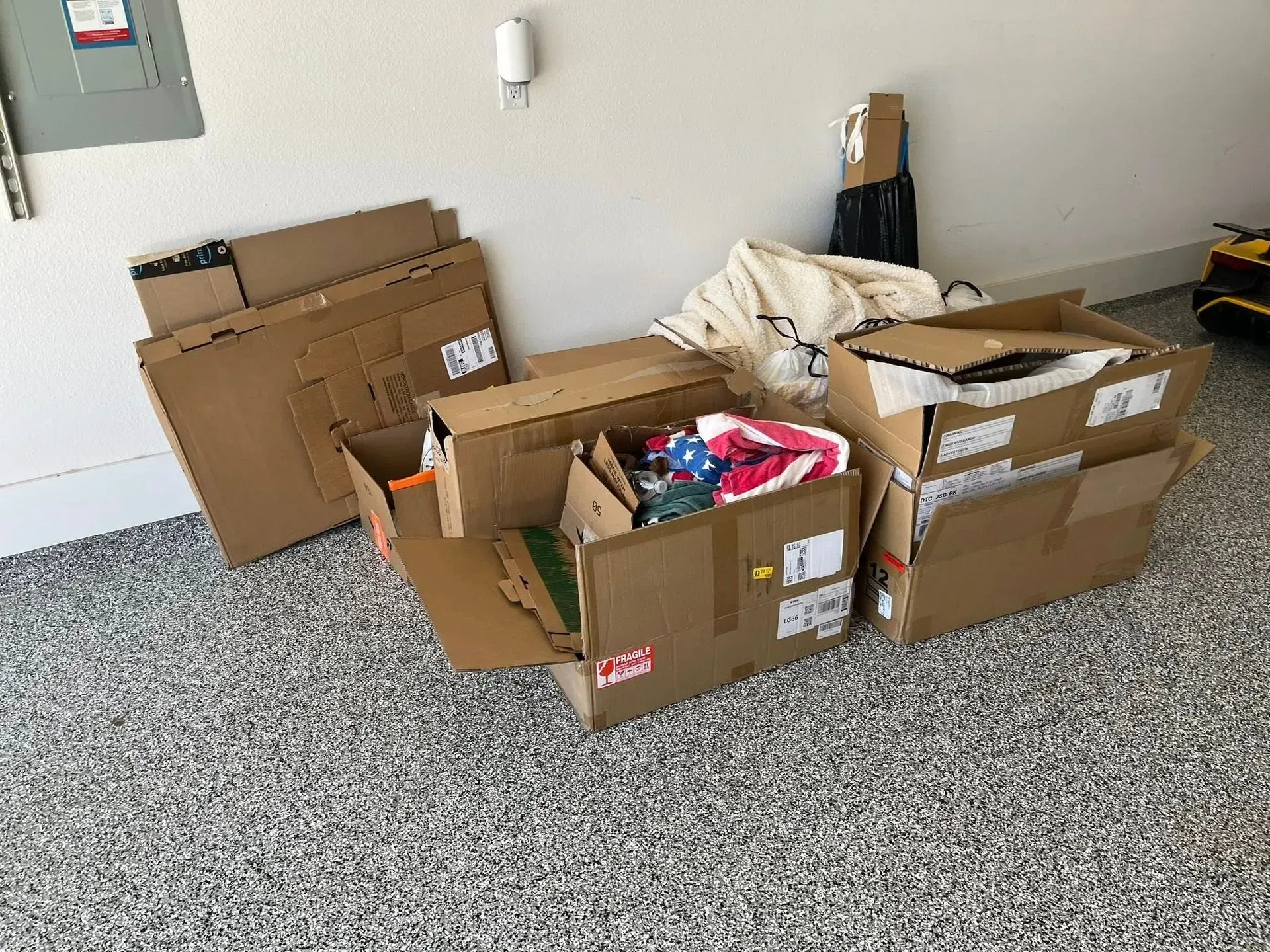 Several open cardboard boxes filled with items sit on a speckled floor in a plain room.