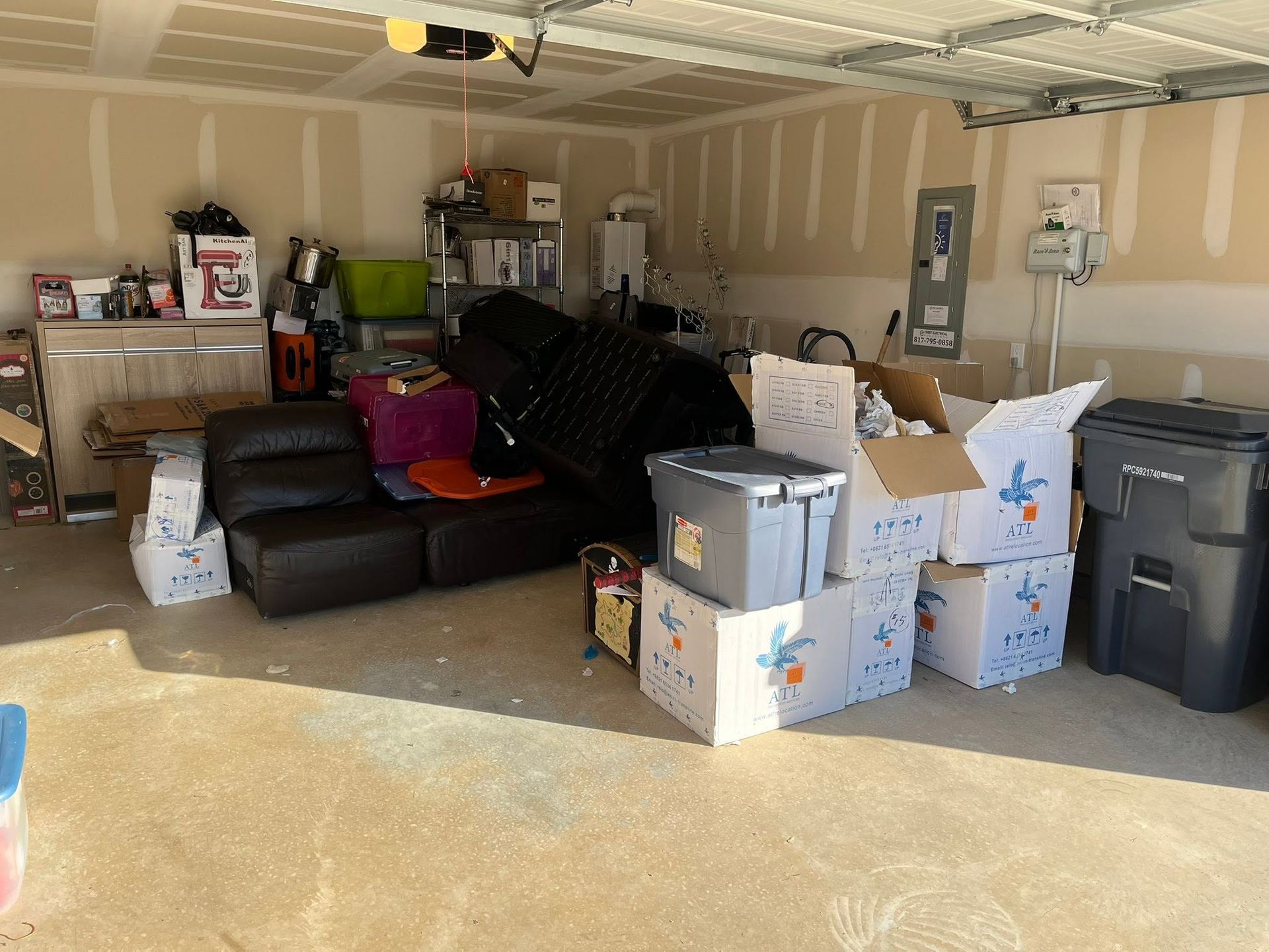 Garage filled with stacked moving boxes, bins, and furniture, including a couch and TV, in a cluttered space