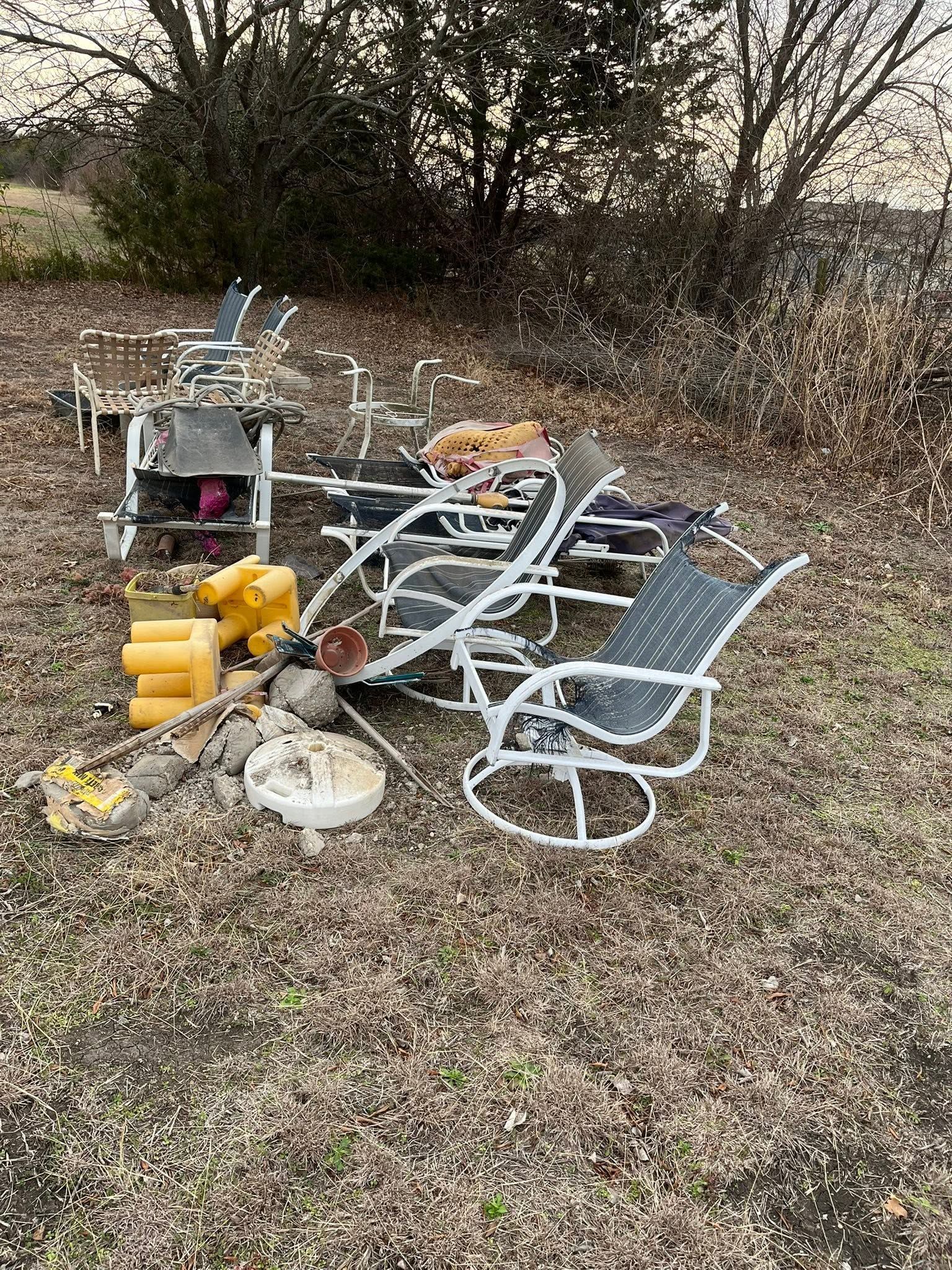 Overturned metal chair and outdoor equipment scattered on a grassy, leaf-covered yard near trees
