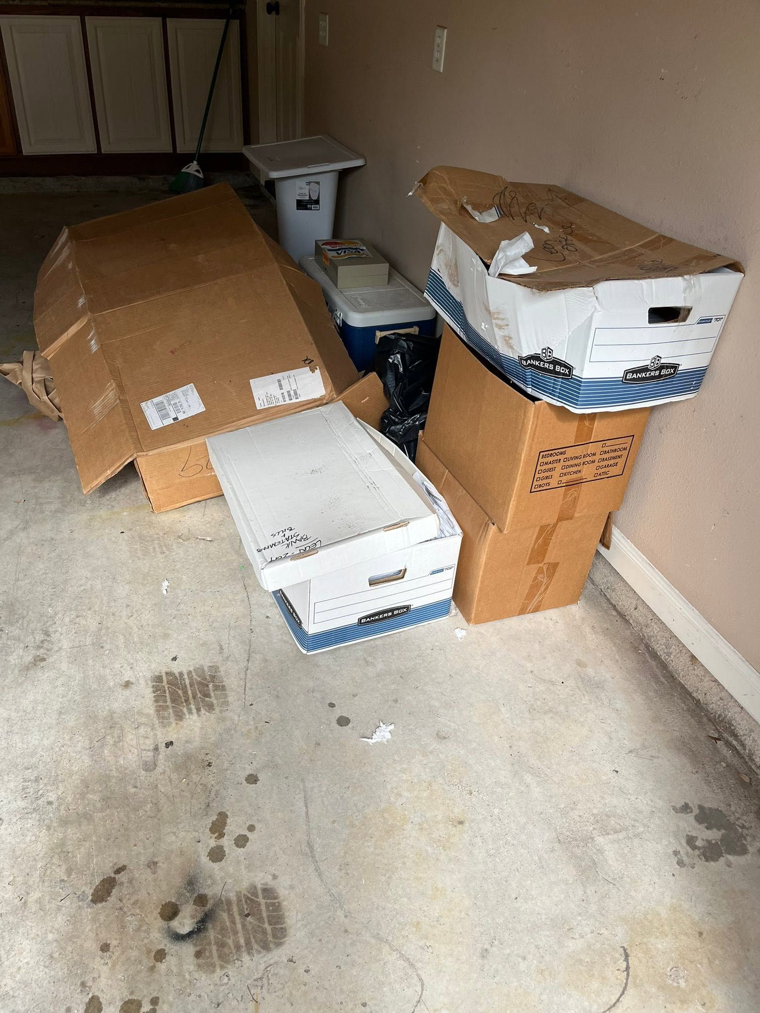Pile of damaged cardboard boxes on a concrete garage floor, with some boxes collapsed and torn open.