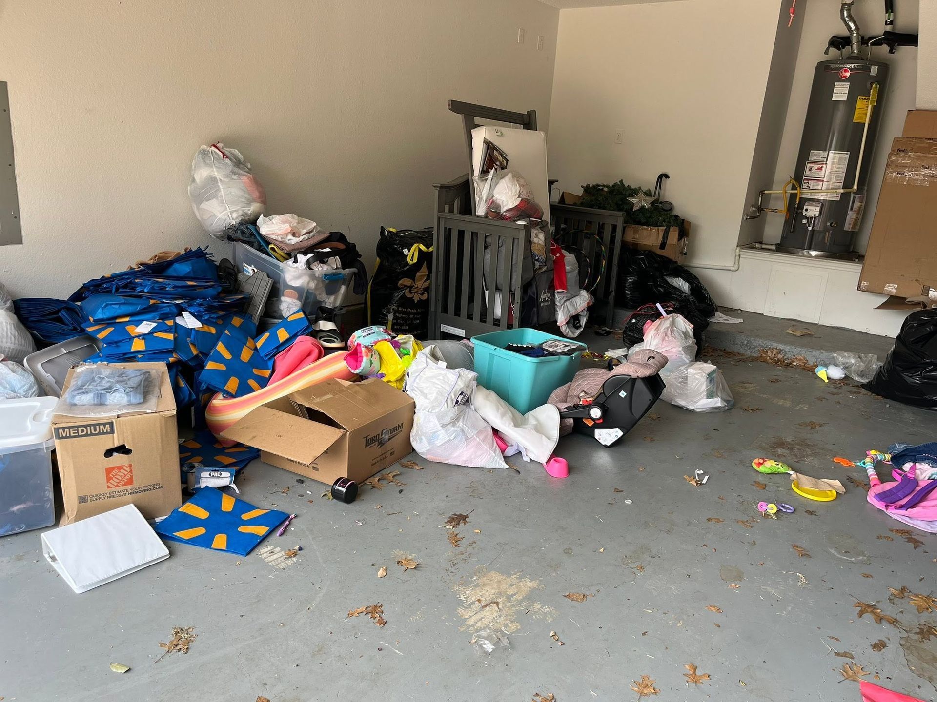 Messy garage with scattered trash bags, boxes, and debris on the floor around stacked items.