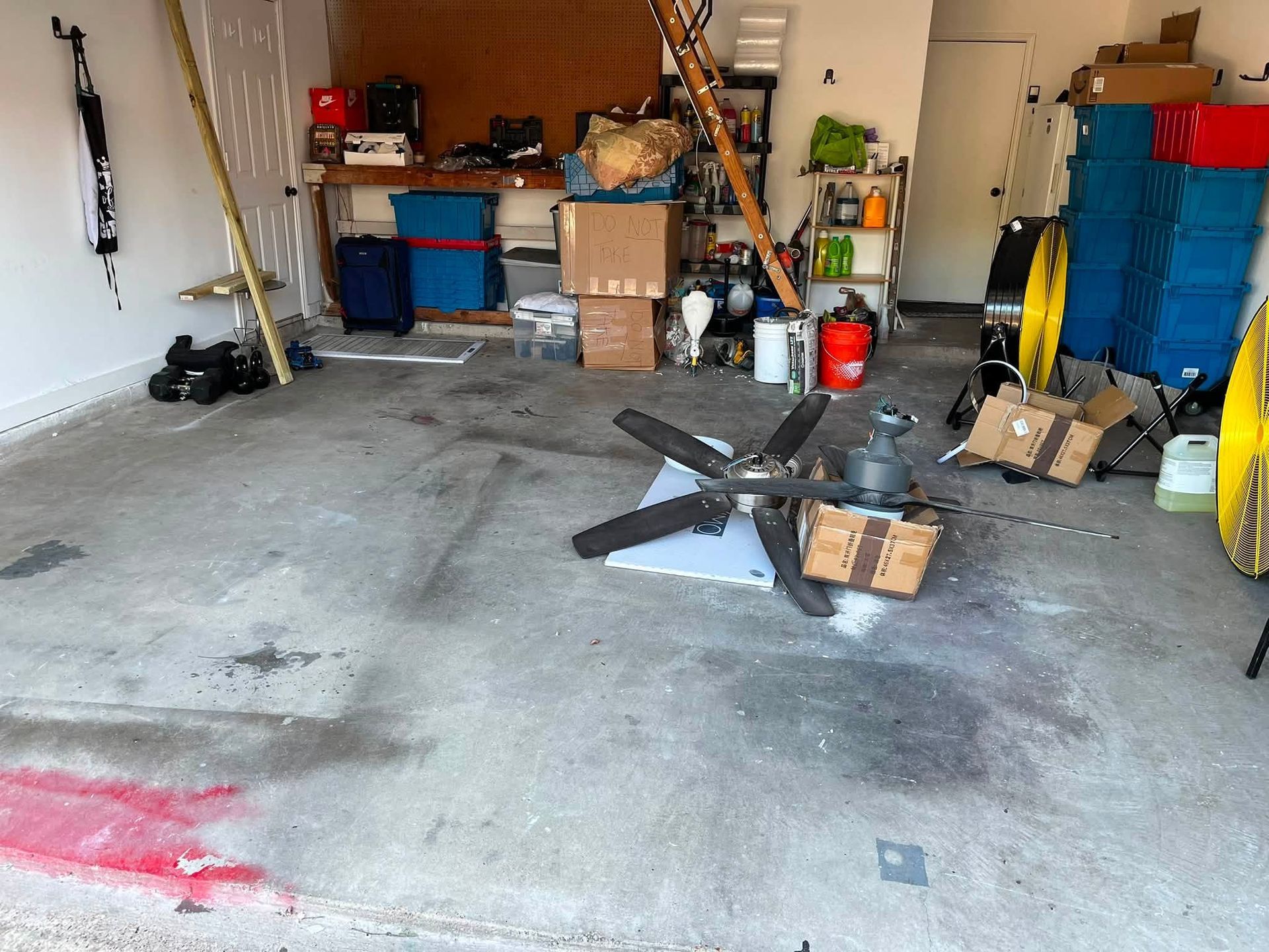 Cluttered garage with tools, storage bins, and fan blades on a concrete floor.