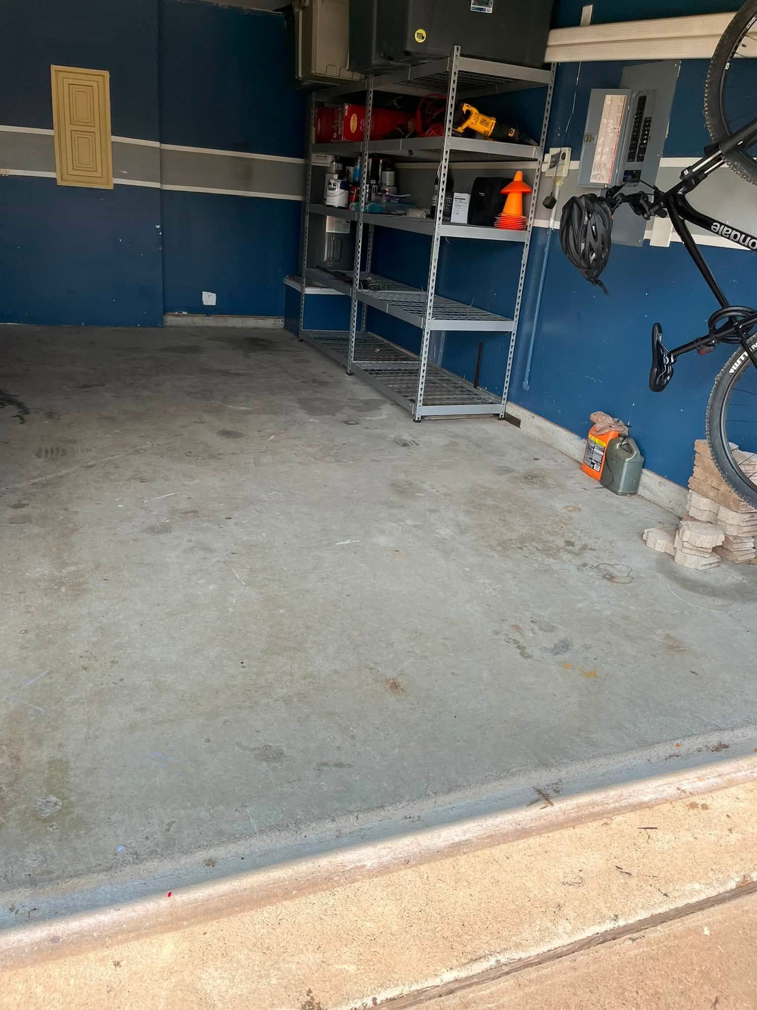 Empty garage with blue walls, concrete floor, metal shelves, and a bicycle-mounted work stand.