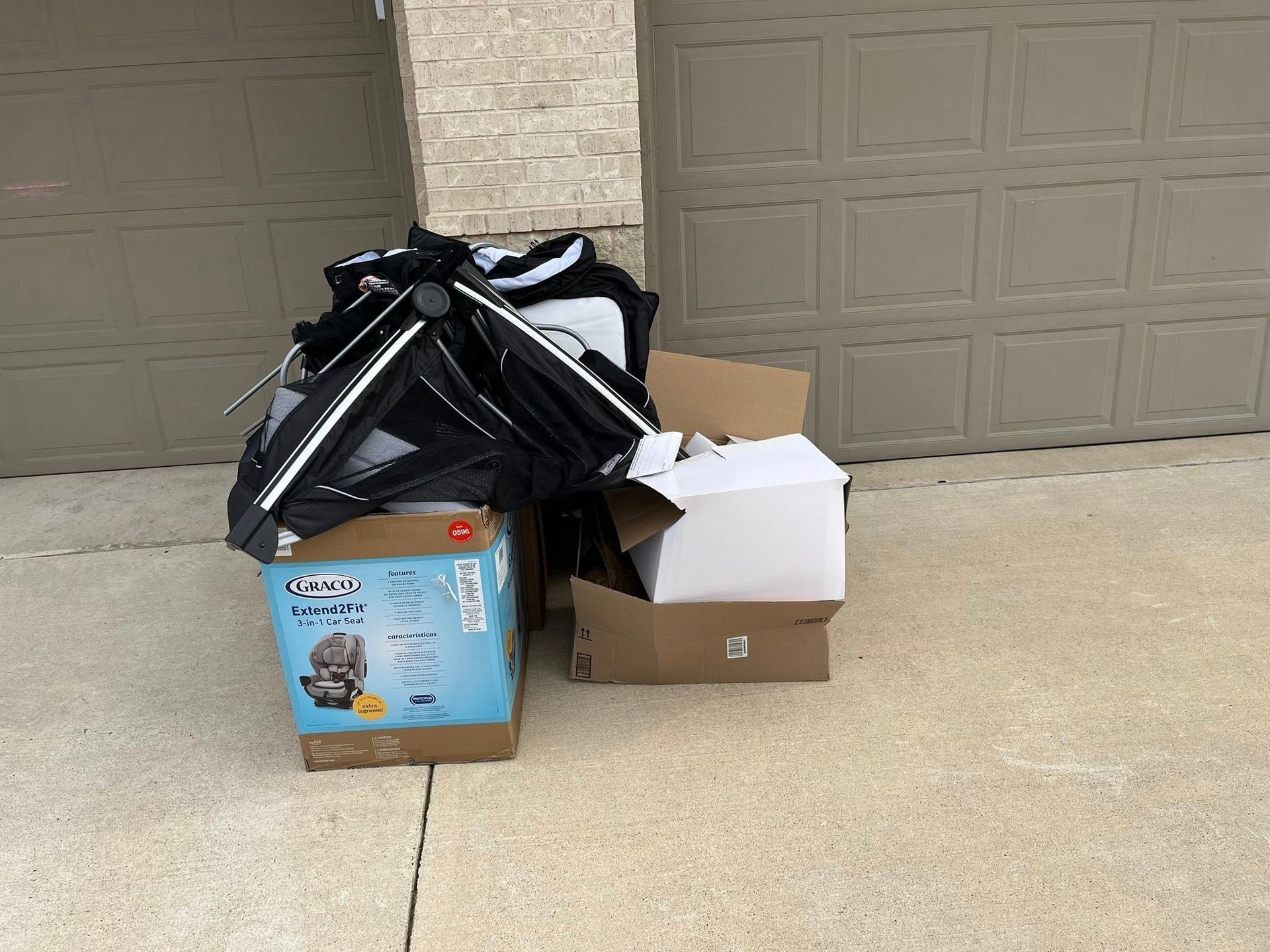 Trash bags and cardboard boxes piled on a driveway in front of closed garage doors.