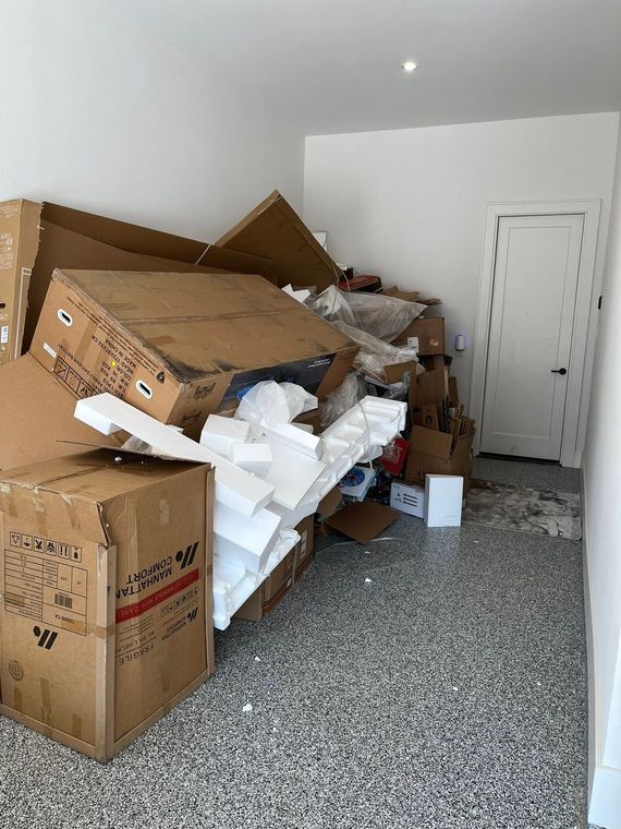 Cluttered room with stacked cardboard boxes, foam packing material, and debris on the floor