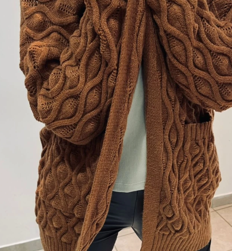 Cárdigan marrón de punto trenzado con bolsillos, abierto. Se vislumbra una camisa blanca y un pantalón negro.