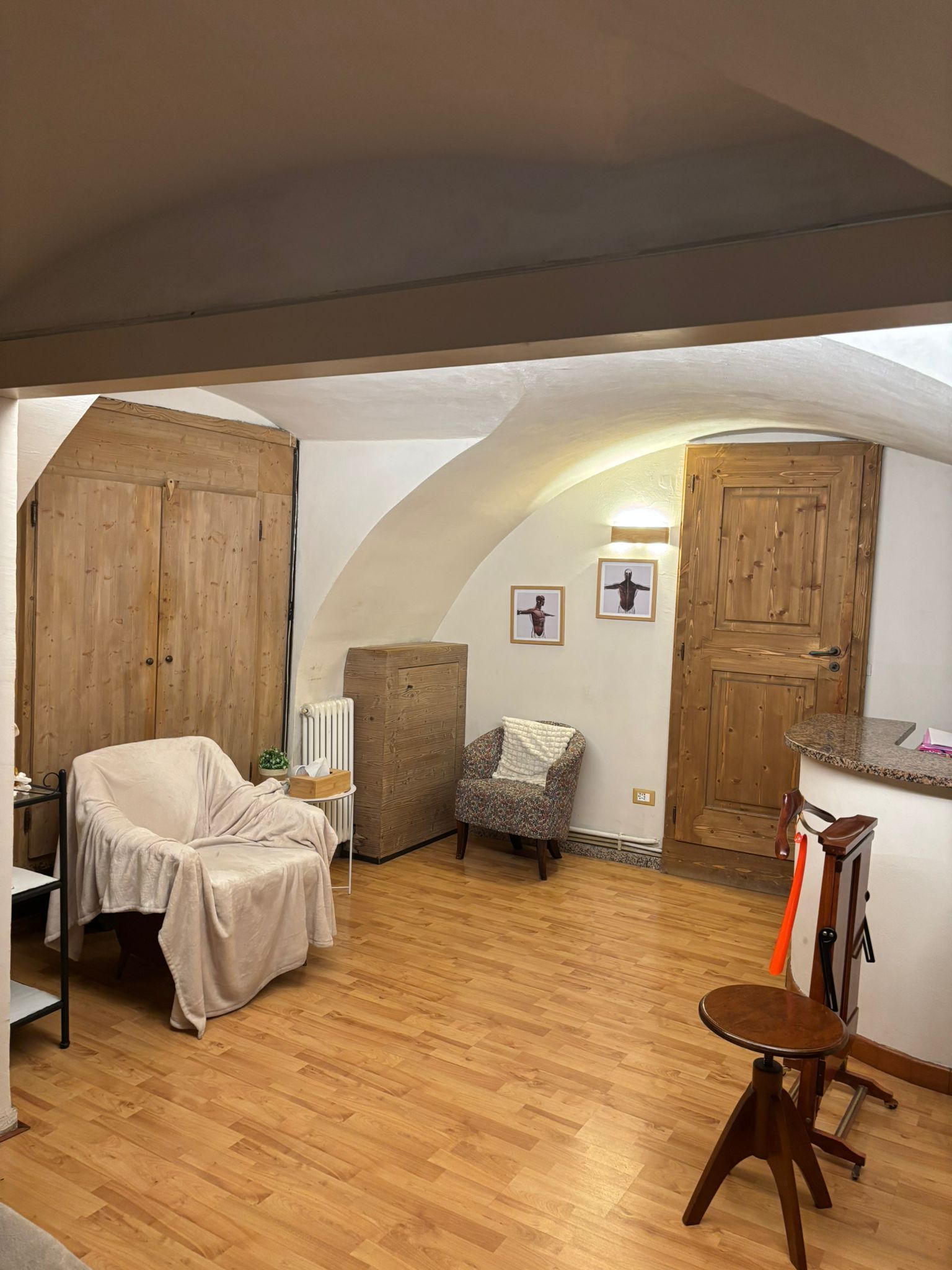 Piccola stanza rustica con pavimento in legno, due sedie, un armadio e una porta sotto un soffitto spiovente.