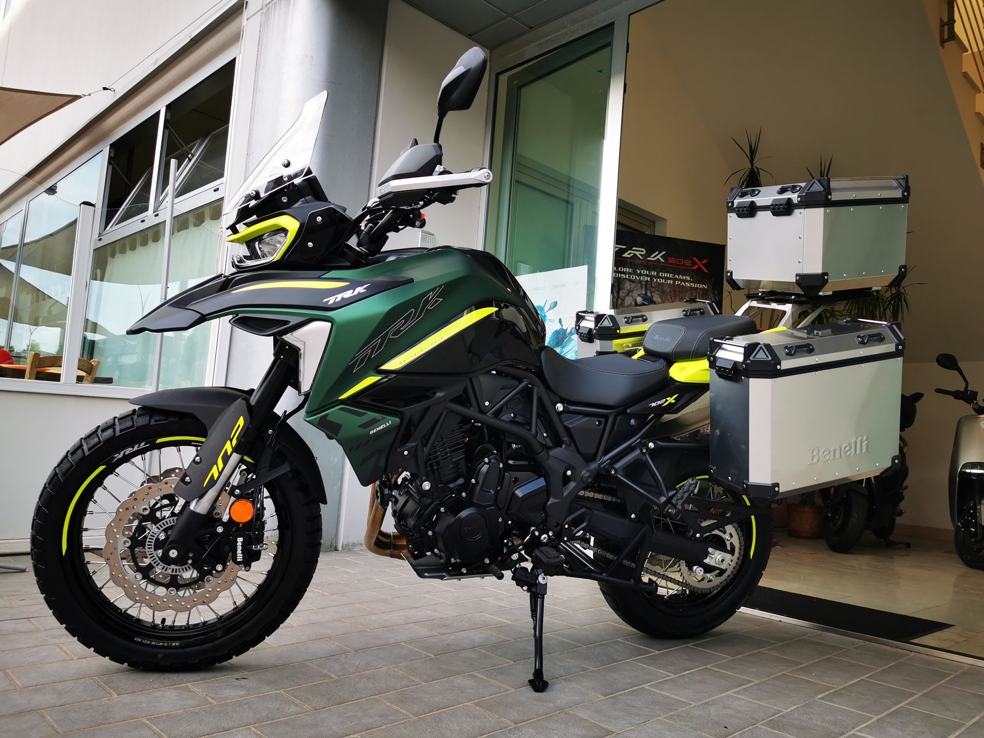 Motocicletta verde e nera con vani portaoggetti argentati, parcheggiata davanti a un edificio.