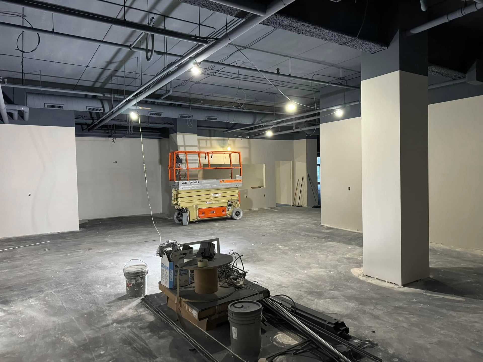 Construction site. Interior view with unfinished walls, machinery, and a lift. Gray and white tones.