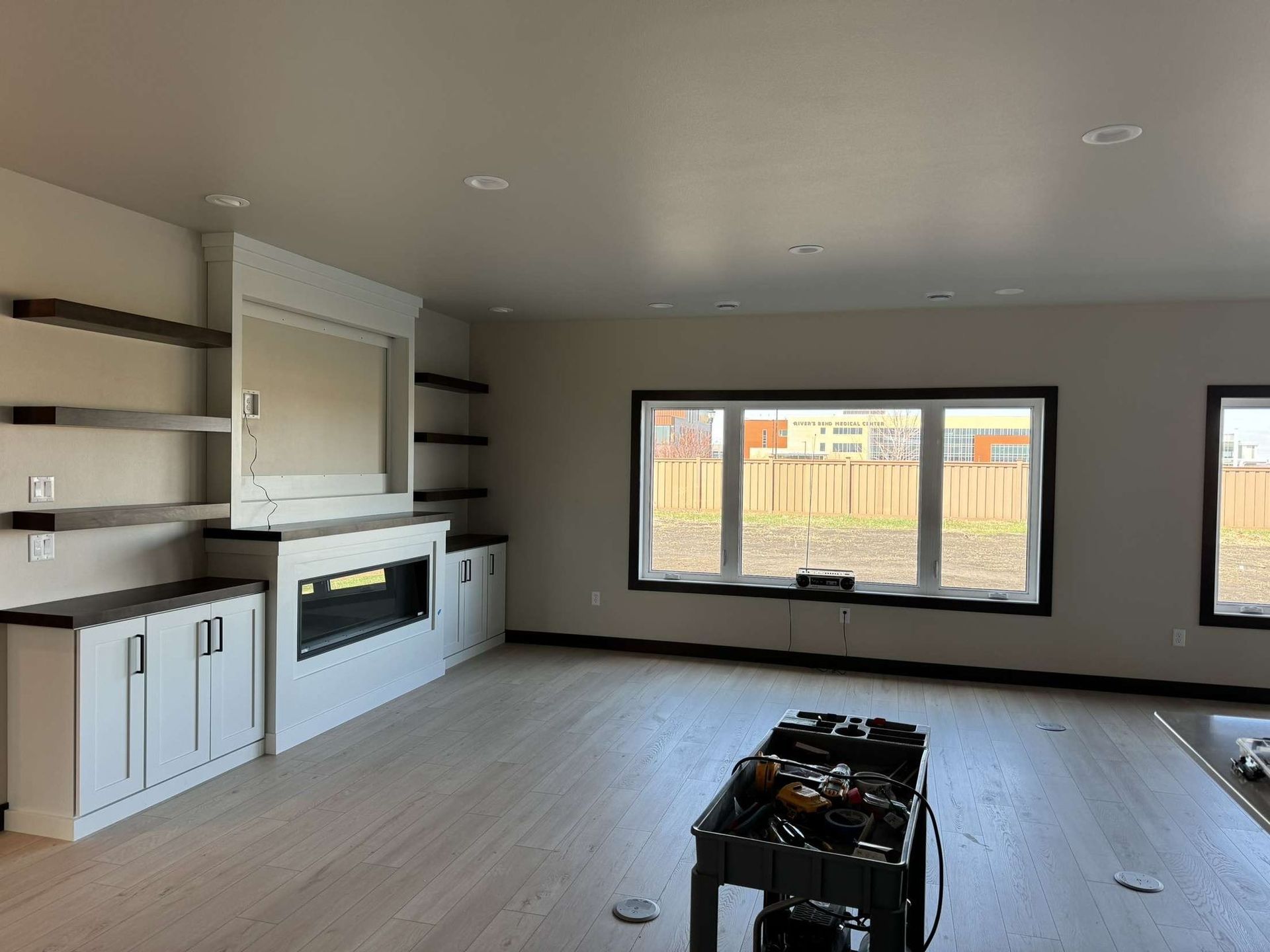 Empty living room with fireplace, built-ins, and large windows; neutral tones.