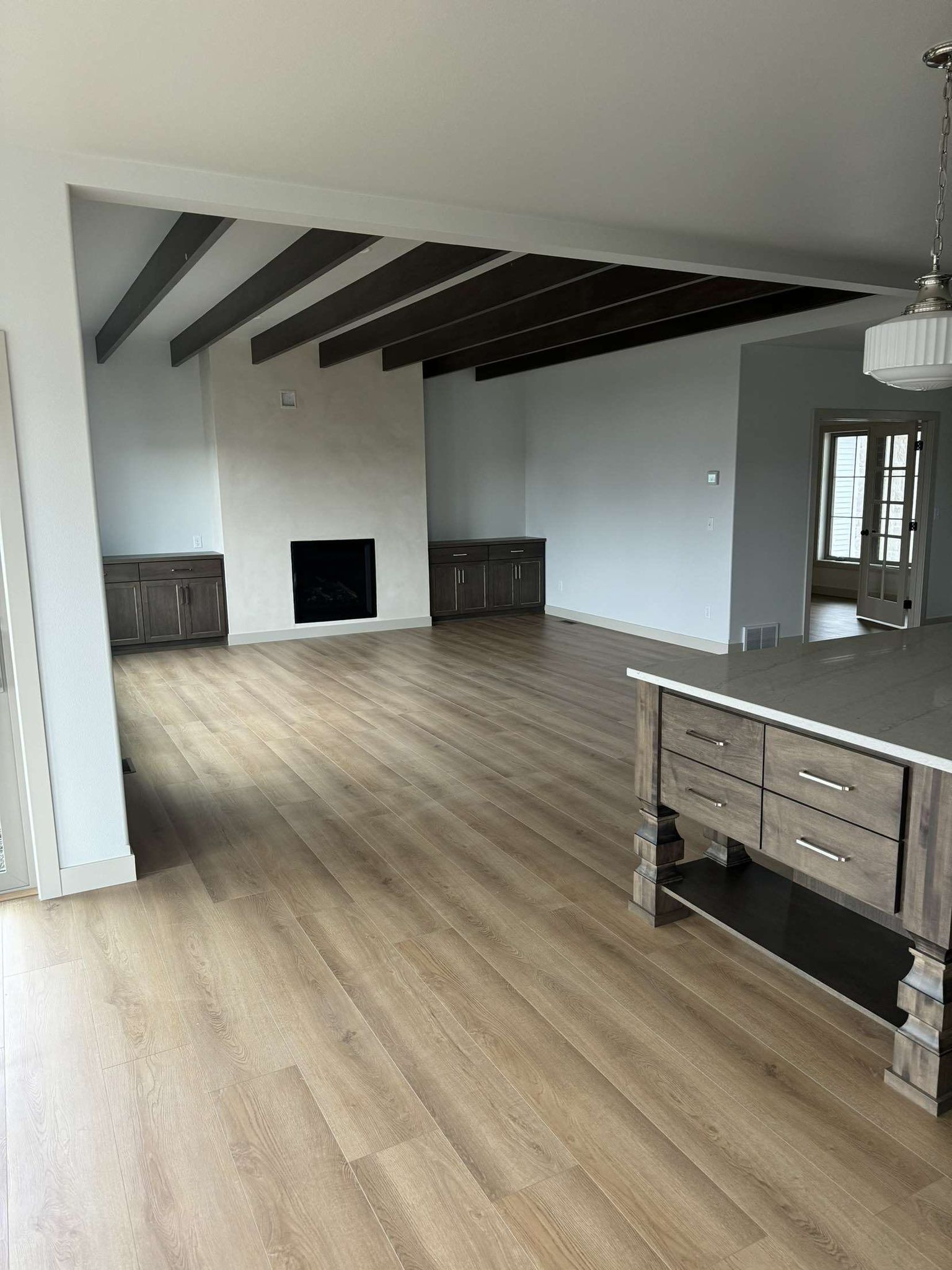 Empty living room with fireplace, exposed beams, and wood flooring.