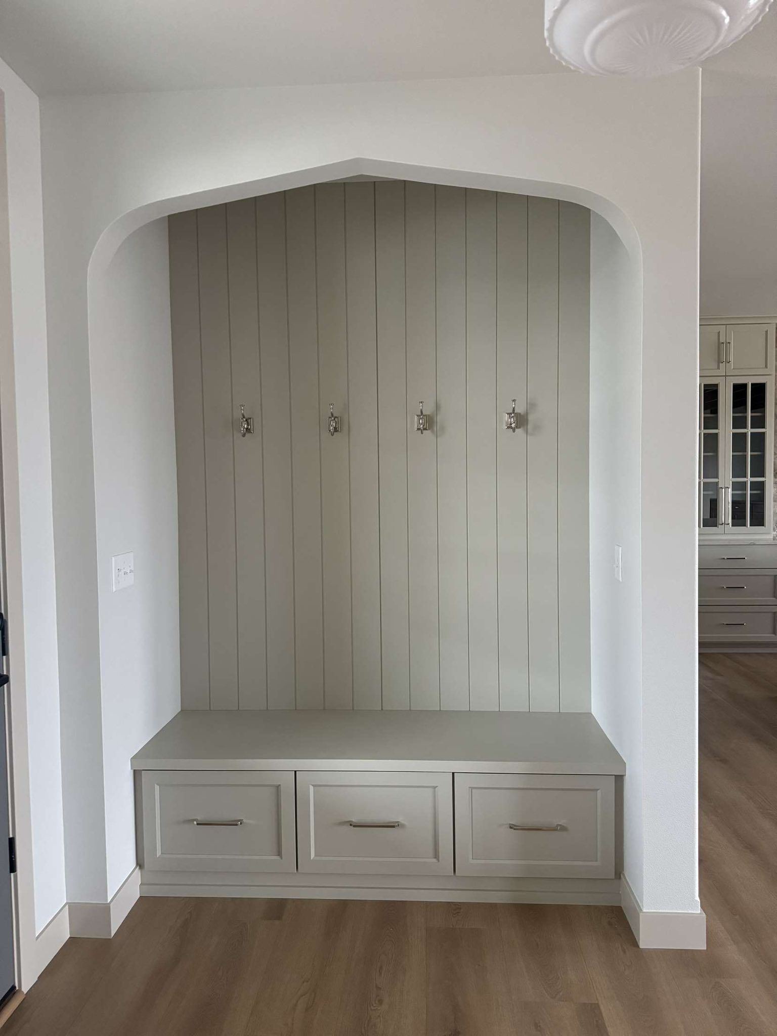 A built-in entryway bench with drawers, hooks, and a curved top, painted gray.