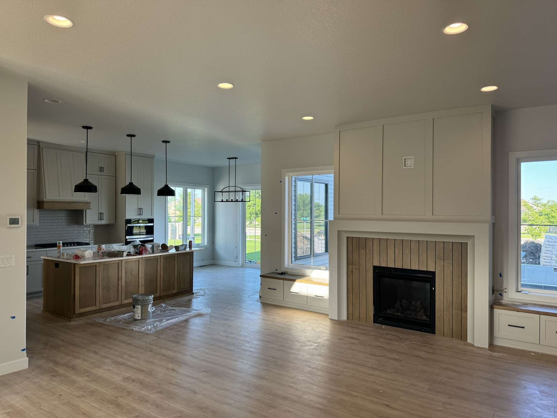 Open-concept home with kitchen, living room, and fireplace. Light wood floors and cabinets, black pendant lights.