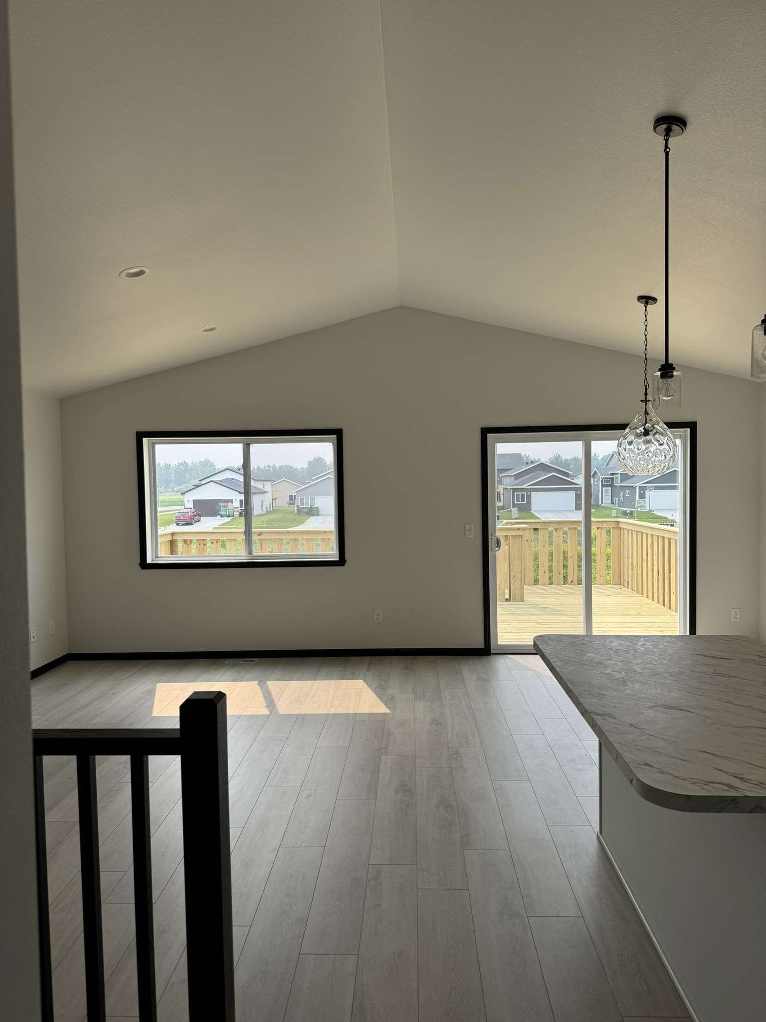 Interior of a modern home with a high ceiling, large window, and a sliding door leading to a deck.