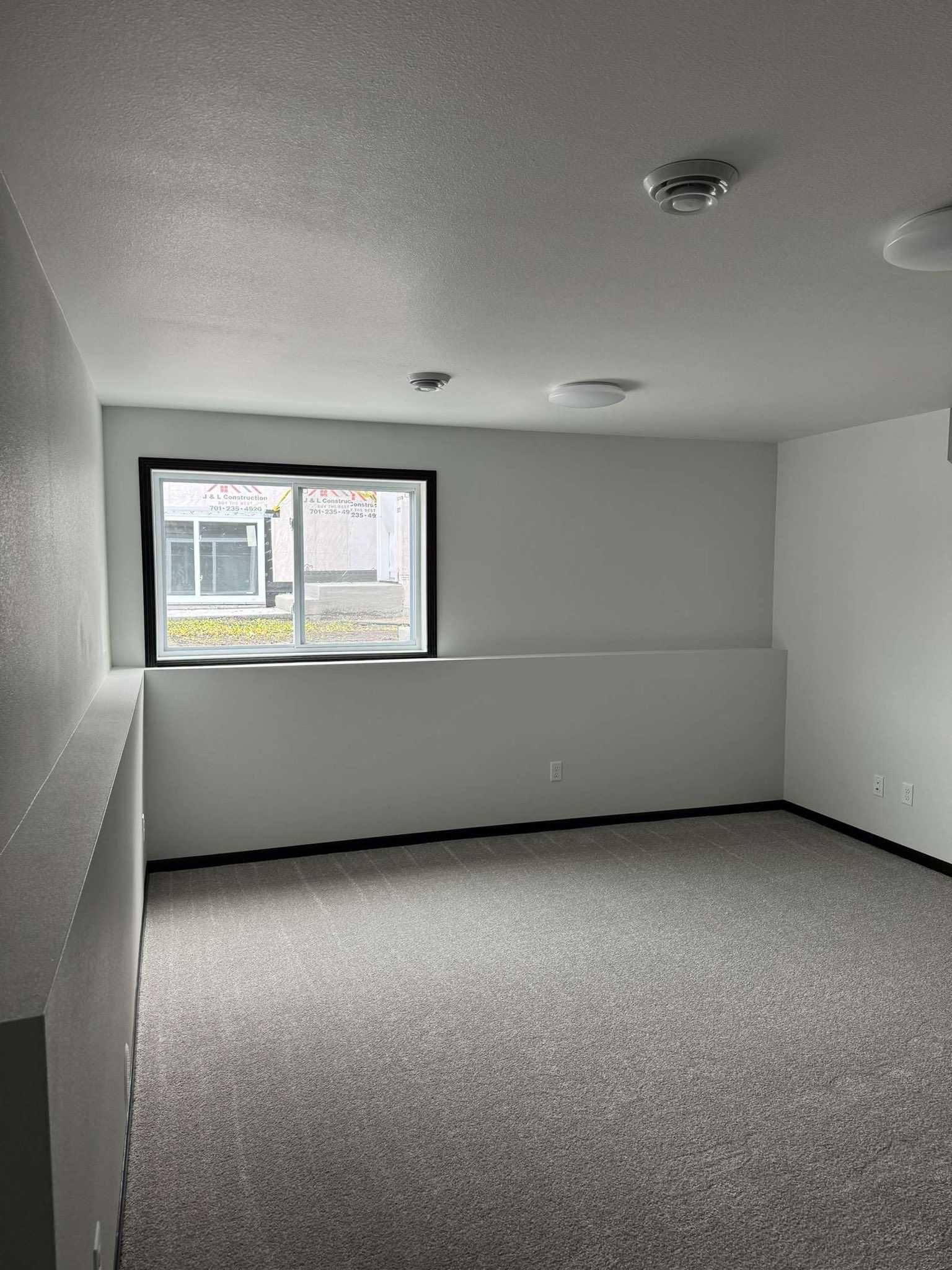 Empty room with white walls, gray carpet, and a window looking outside.