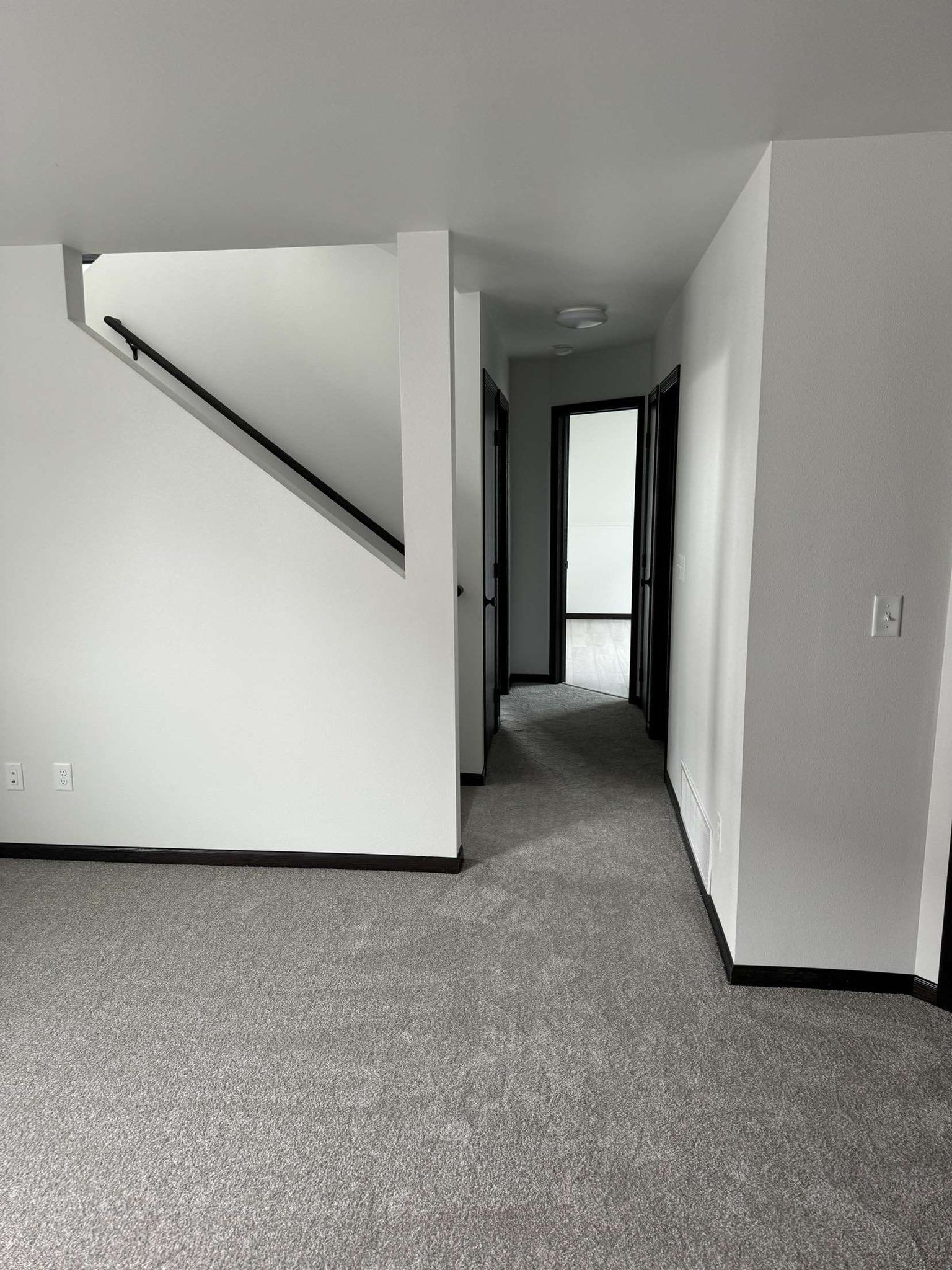 Hallway with carpet, white walls, and dark door frames. Stairs on the left.