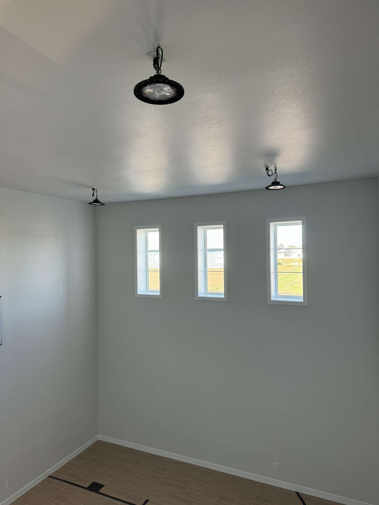 Three small windows and three ceiling lights in a room with light gray walls and beige floor.