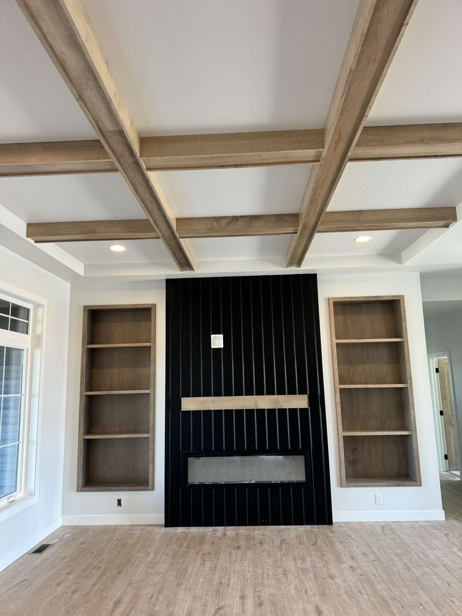 Living room with black fireplace, built-in bookshelves, and light wooden ceiling beams.