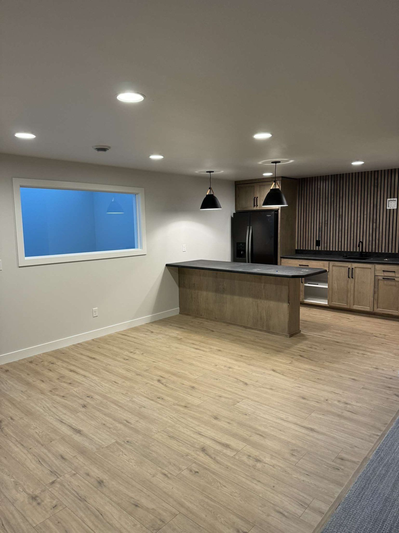 Empty kitchen with wood cabinets, island, black appliances, and window with blue space.