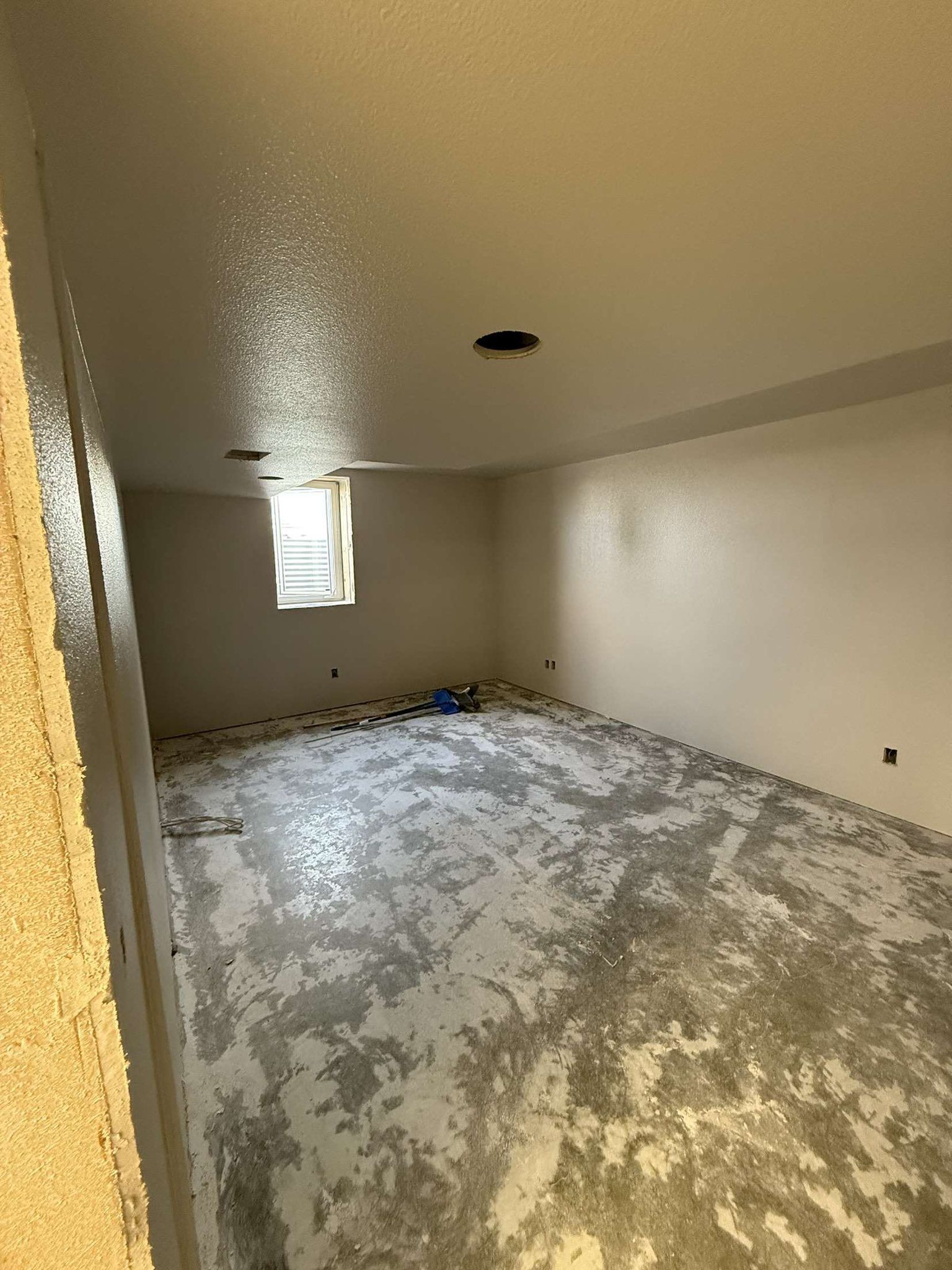 Empty room with unfinished concrete floor and painted walls, small window, and ceiling lights.