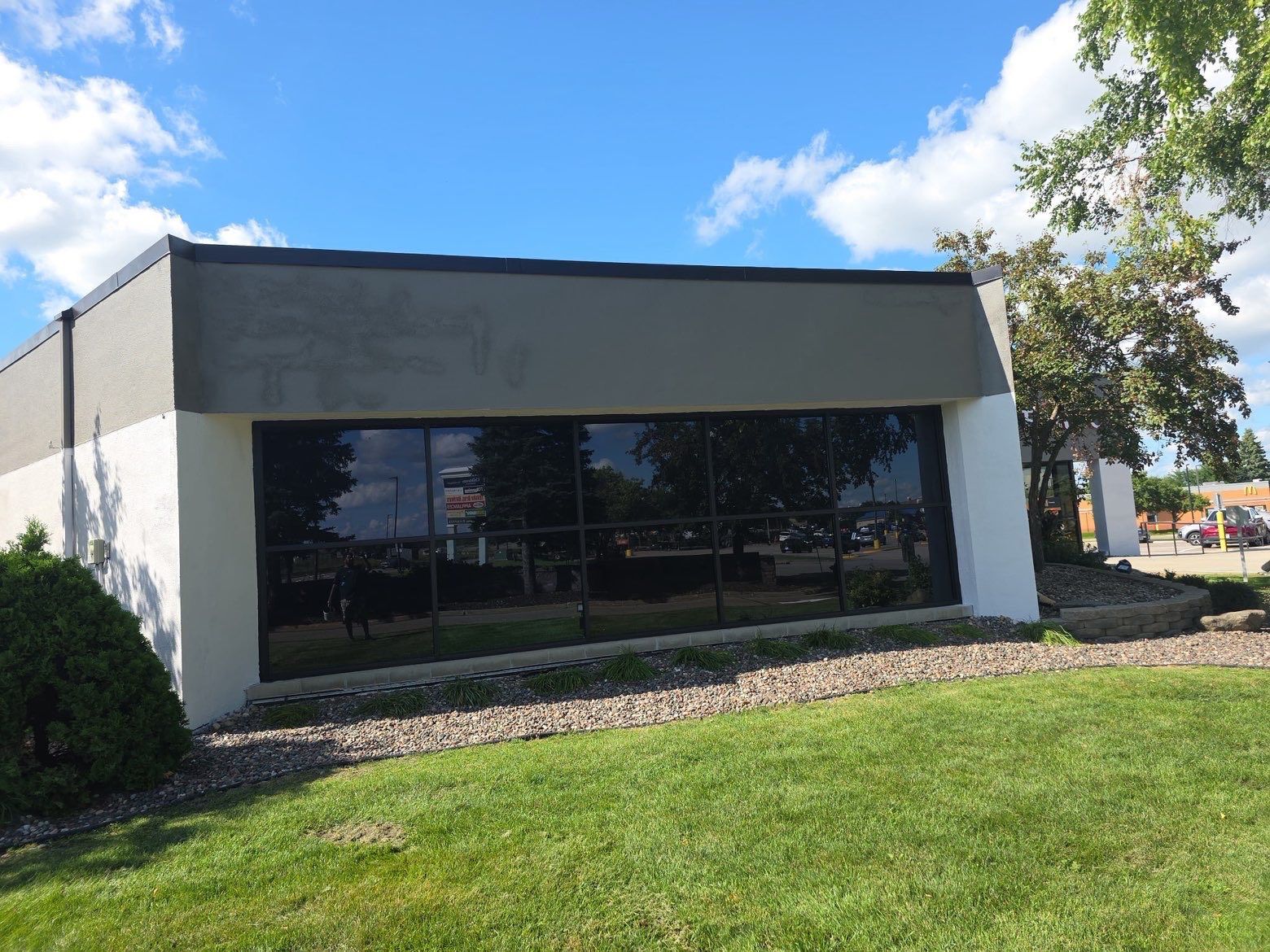 Exterior of a building with large windows, gray and white walls, and a grassy lawn under a blue sky.