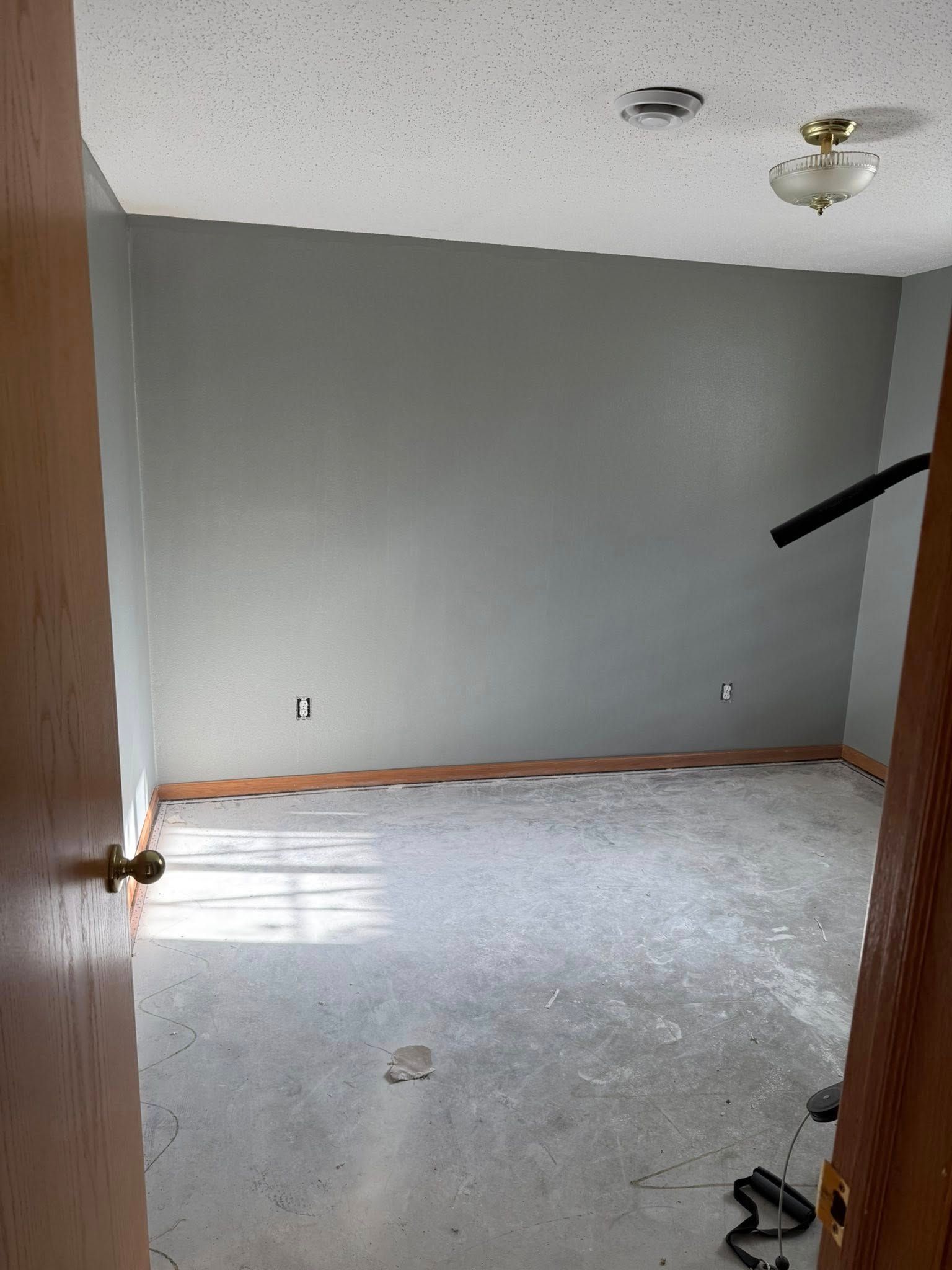 Empty room with gray walls, unfinished floor, and open door.