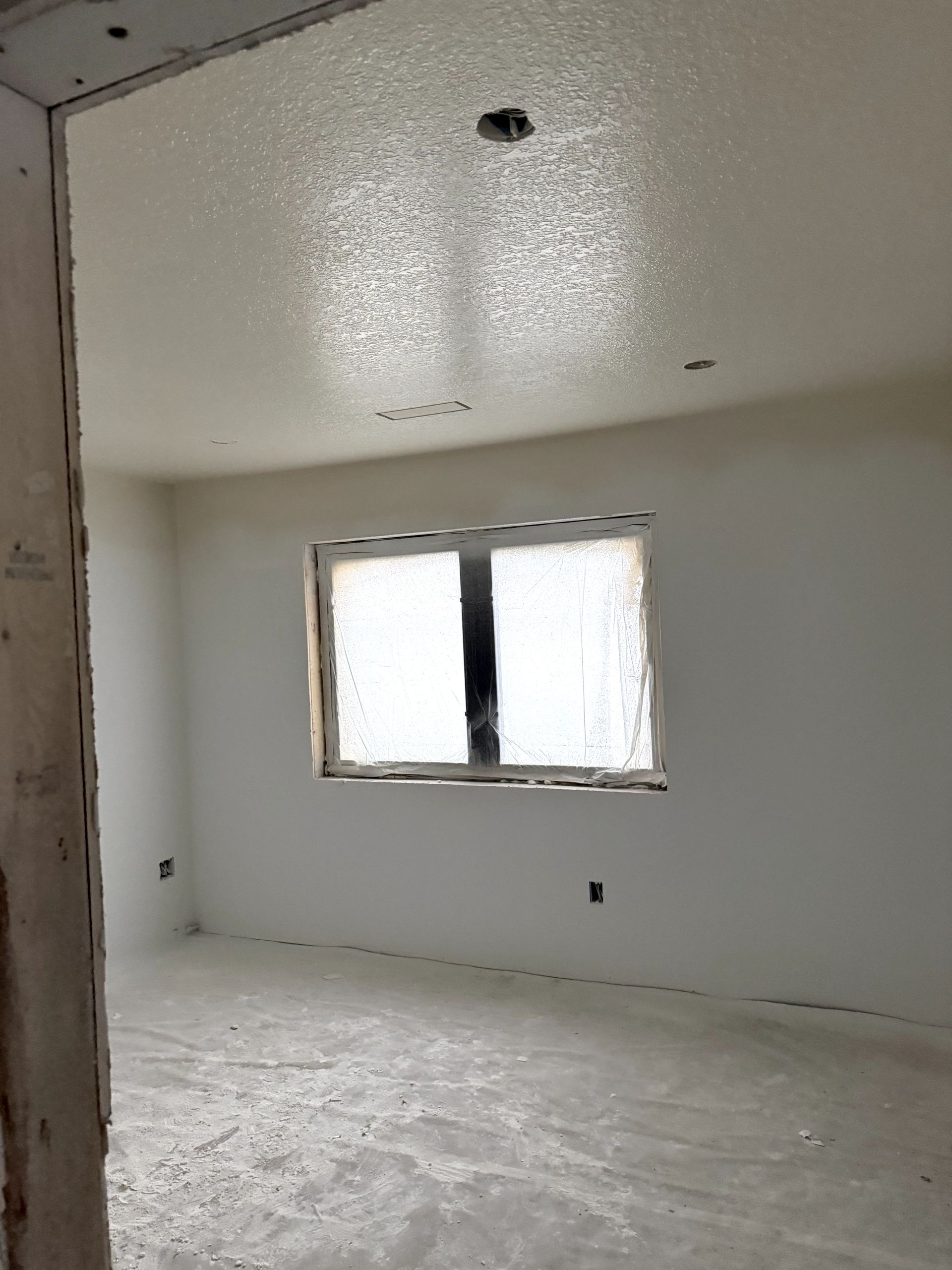 Narrow hallway under construction, light-colored walls, unfinished ceiling, window on right, doorway at end.