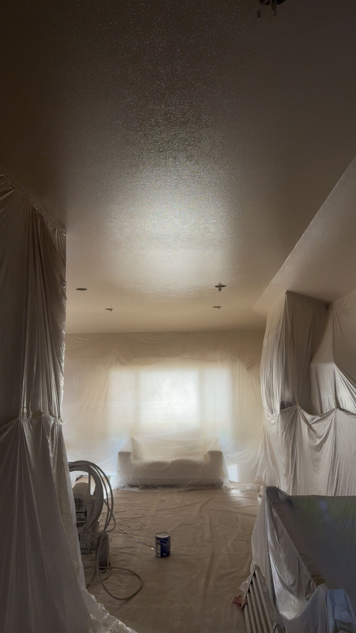 Interior wall with exposed insulation between wooden studs, plastic sheeting on concrete floor.
