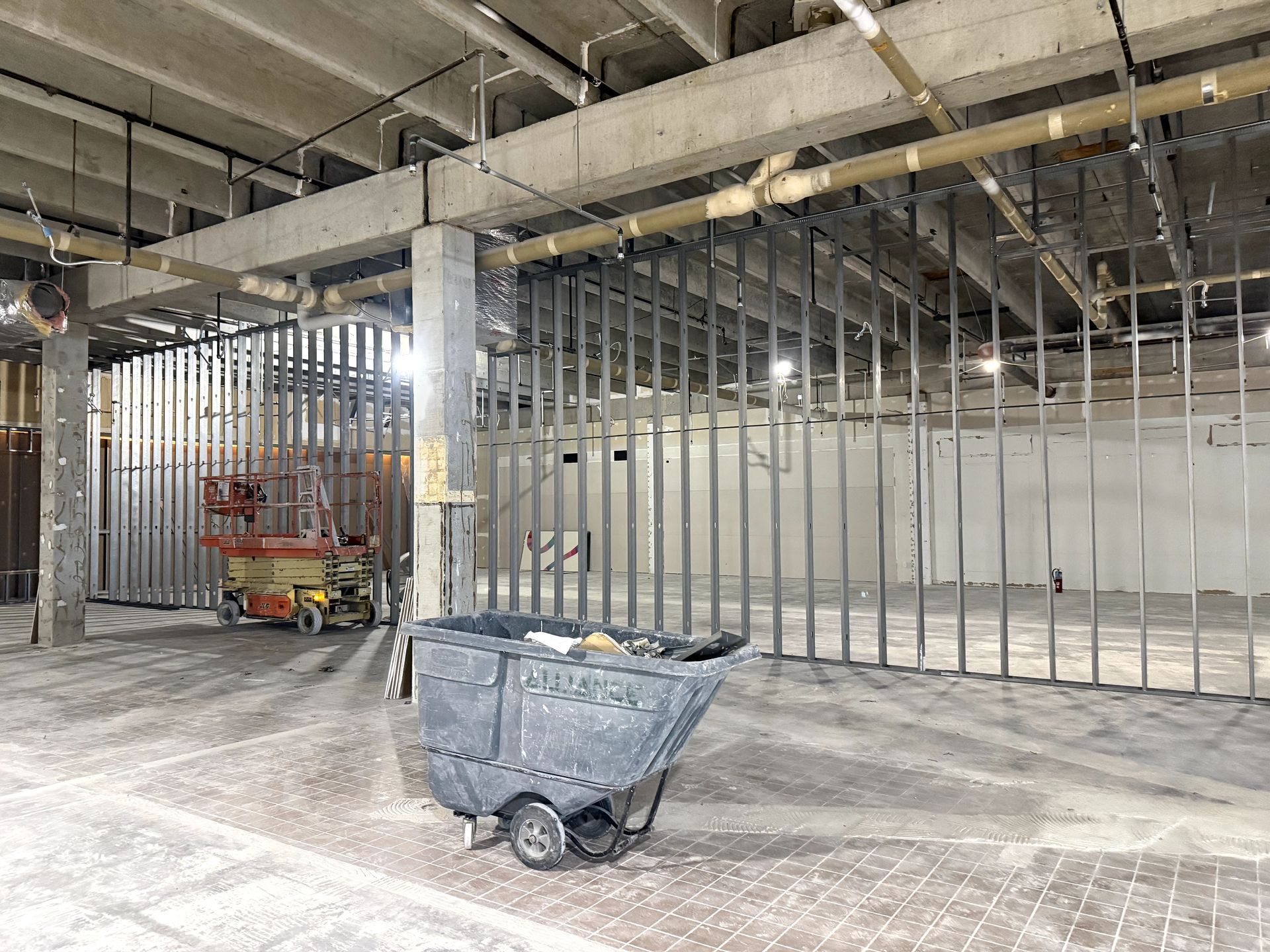 Narrow hallway under construction, light-colored walls, unfinished ceiling, window on right, doorway at end.
