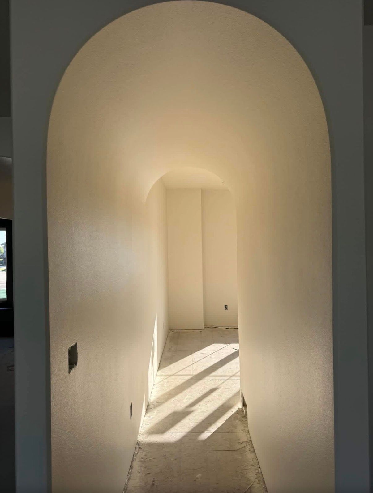 Room with tan walls, cement floor, ceiling light, smoke detector, and standing fan. Door on right.