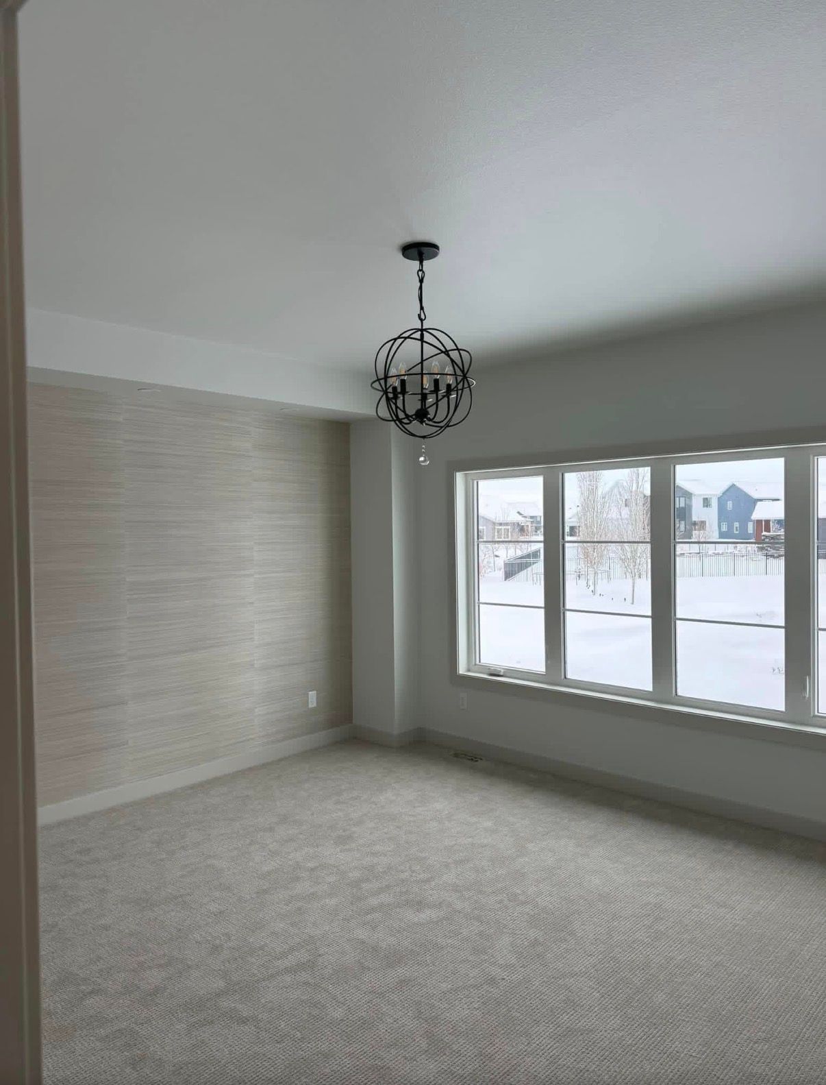 Room with tan walls, cement floor, ceiling light, smoke detector, and standing fan. Door on right.