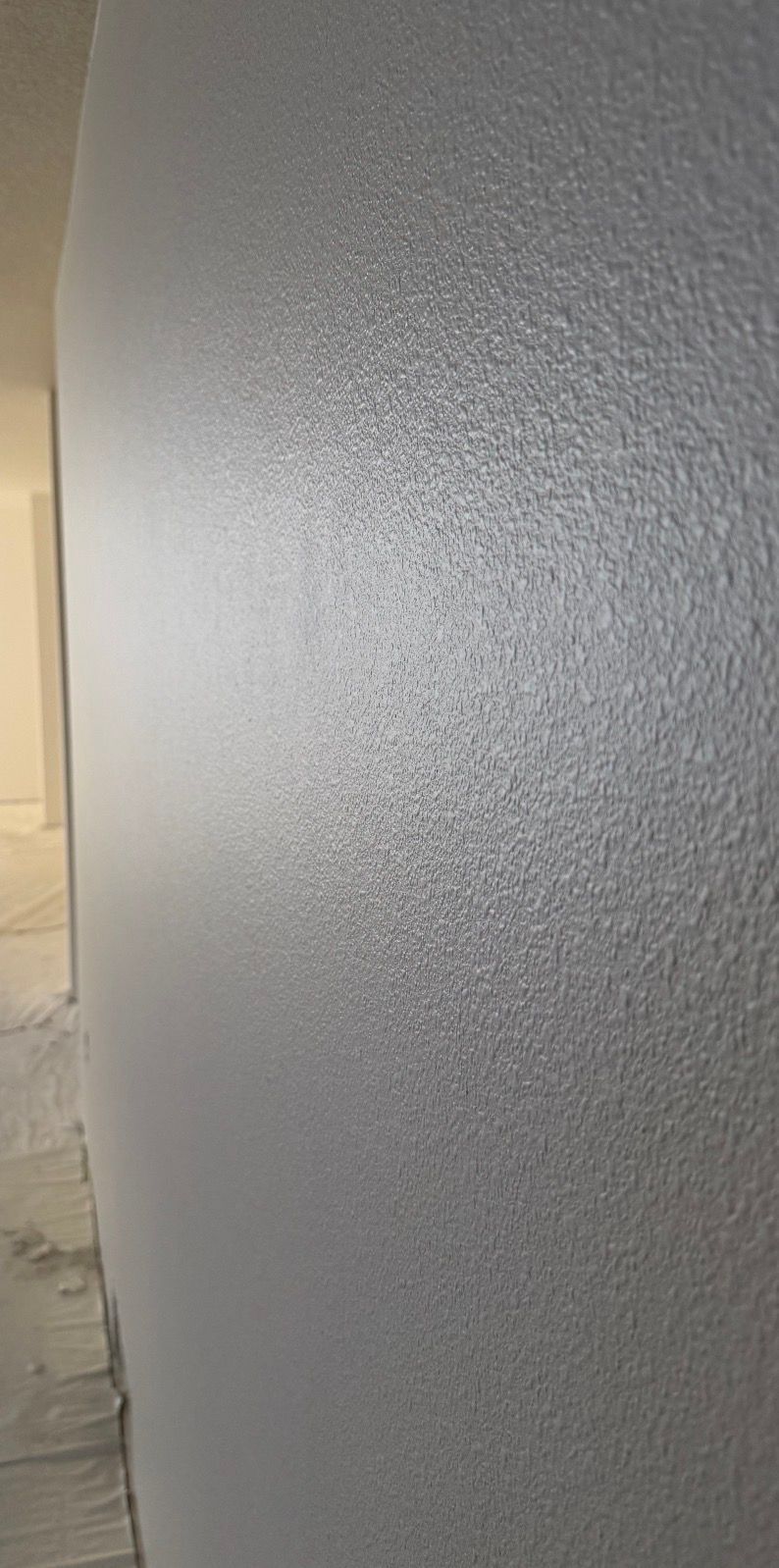 Man on a ladder spraying ceiling with a speckled texture. White walls, interior setting.