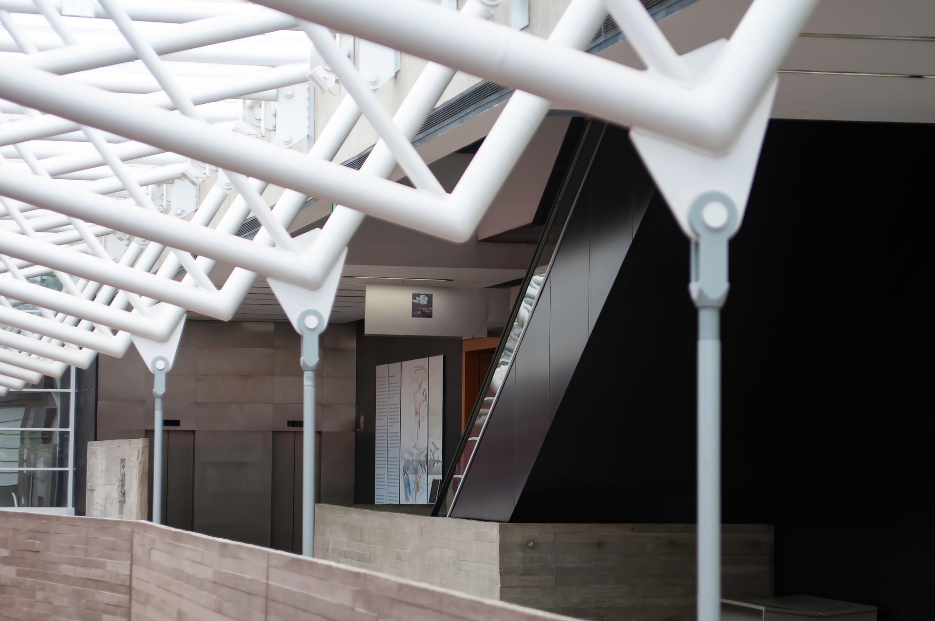 Covered outdoor walkway with white geometric beams and stairs leading to a building entrance