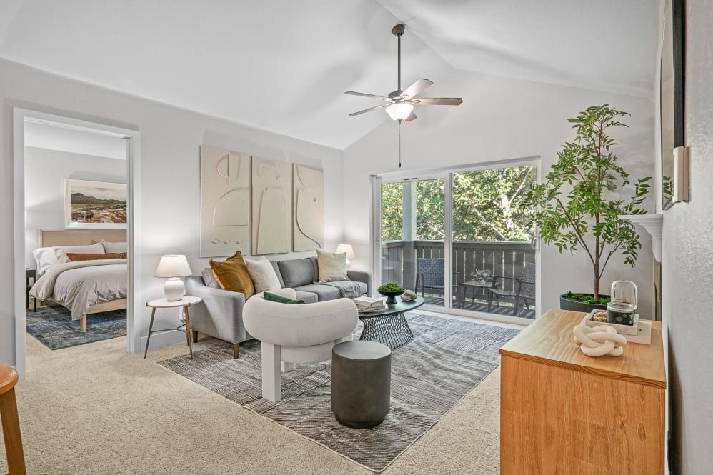 Living room with gray sofa, abstract art, and sliding door to balcony overlooking trees. Bedroom visible.