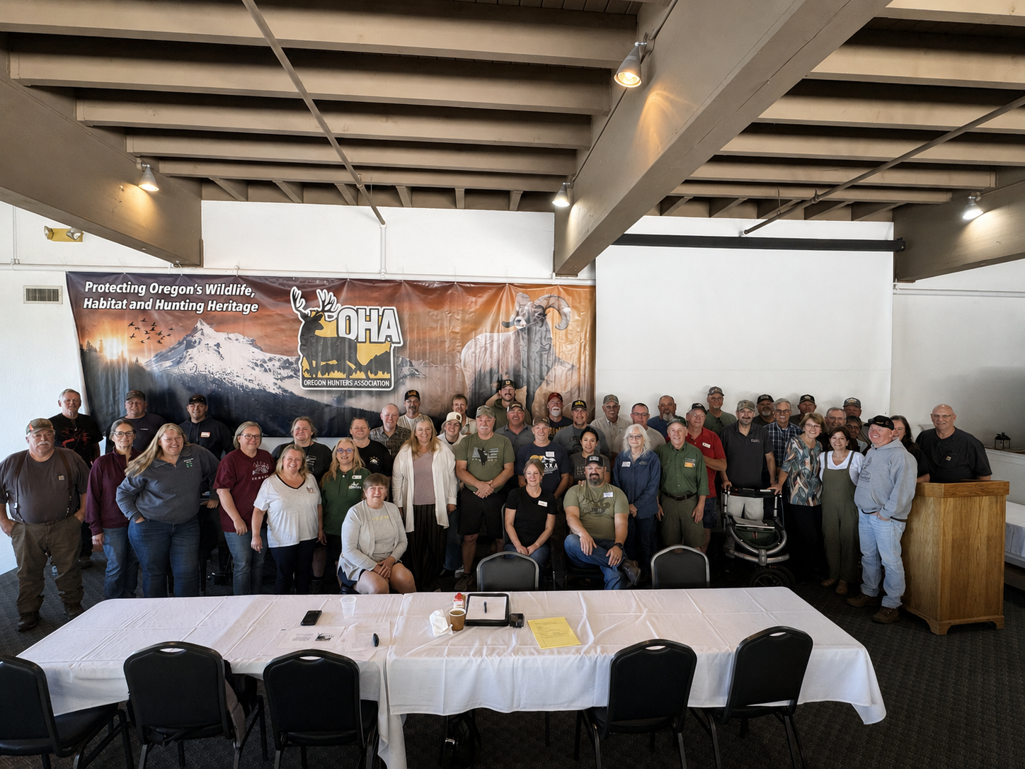 Large group posing in a banquet hall behind a long table with a banner and podium in the background