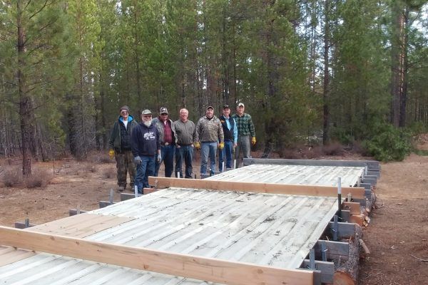 People standing beside a long wooden bridge under construction in a forest.