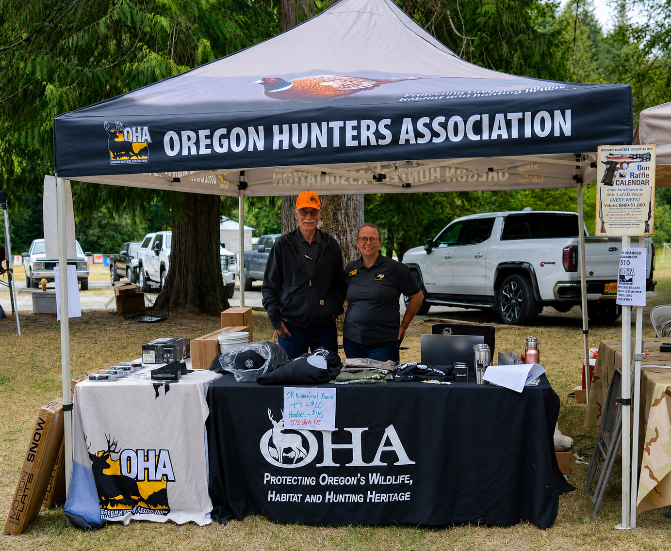 Oregon Hunters Association booth under a black canopy, with two people standing behind a display table outdoors.