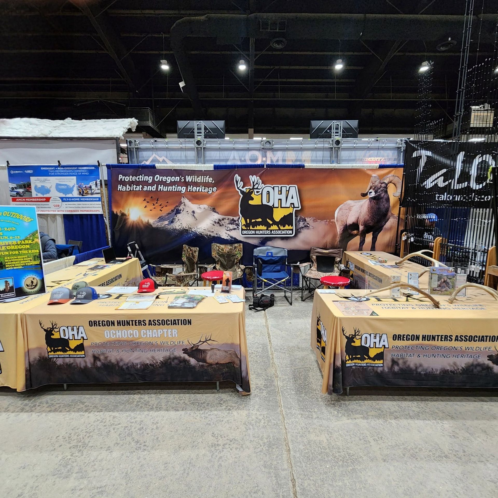 Con expo booth with camo banners, deer and turkey graphics, and hunting gear on display.